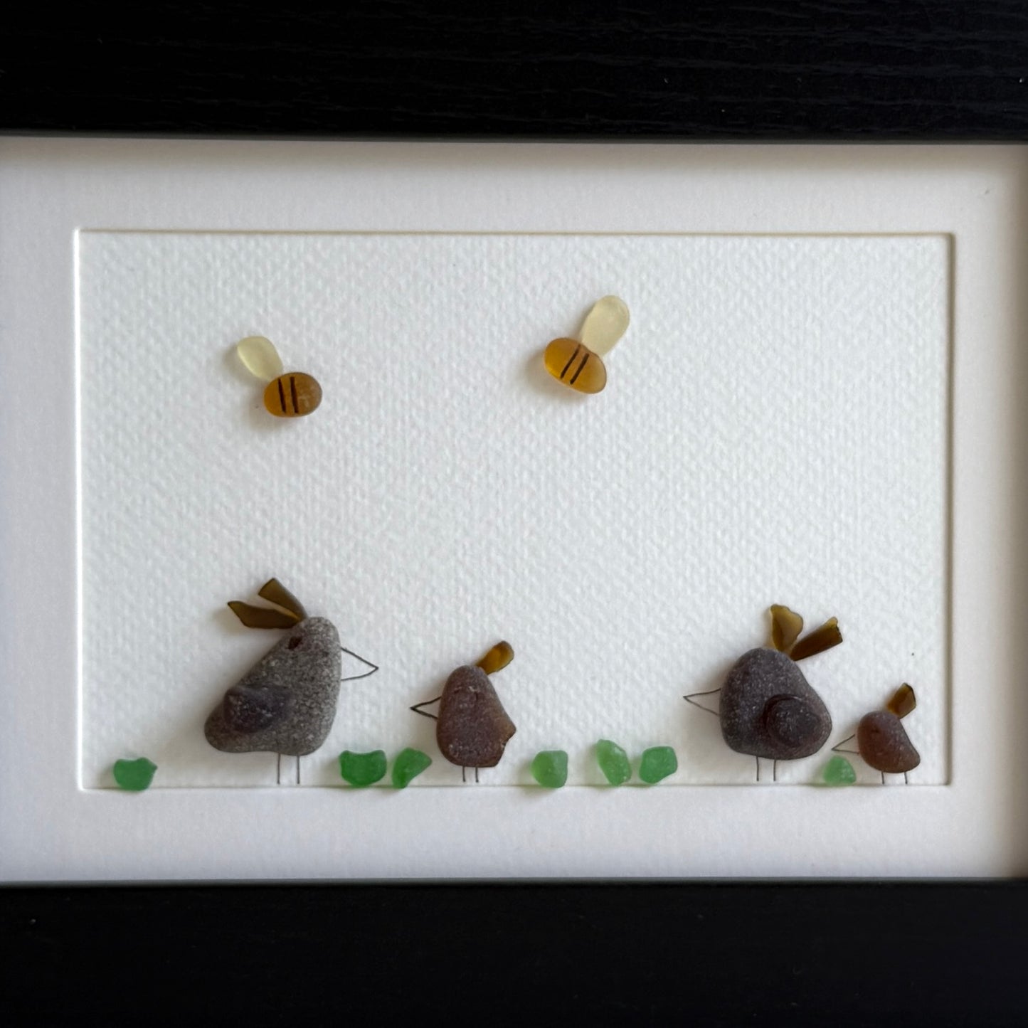Framed sea glass artwork of hens and chickens on a white background with a black frame.