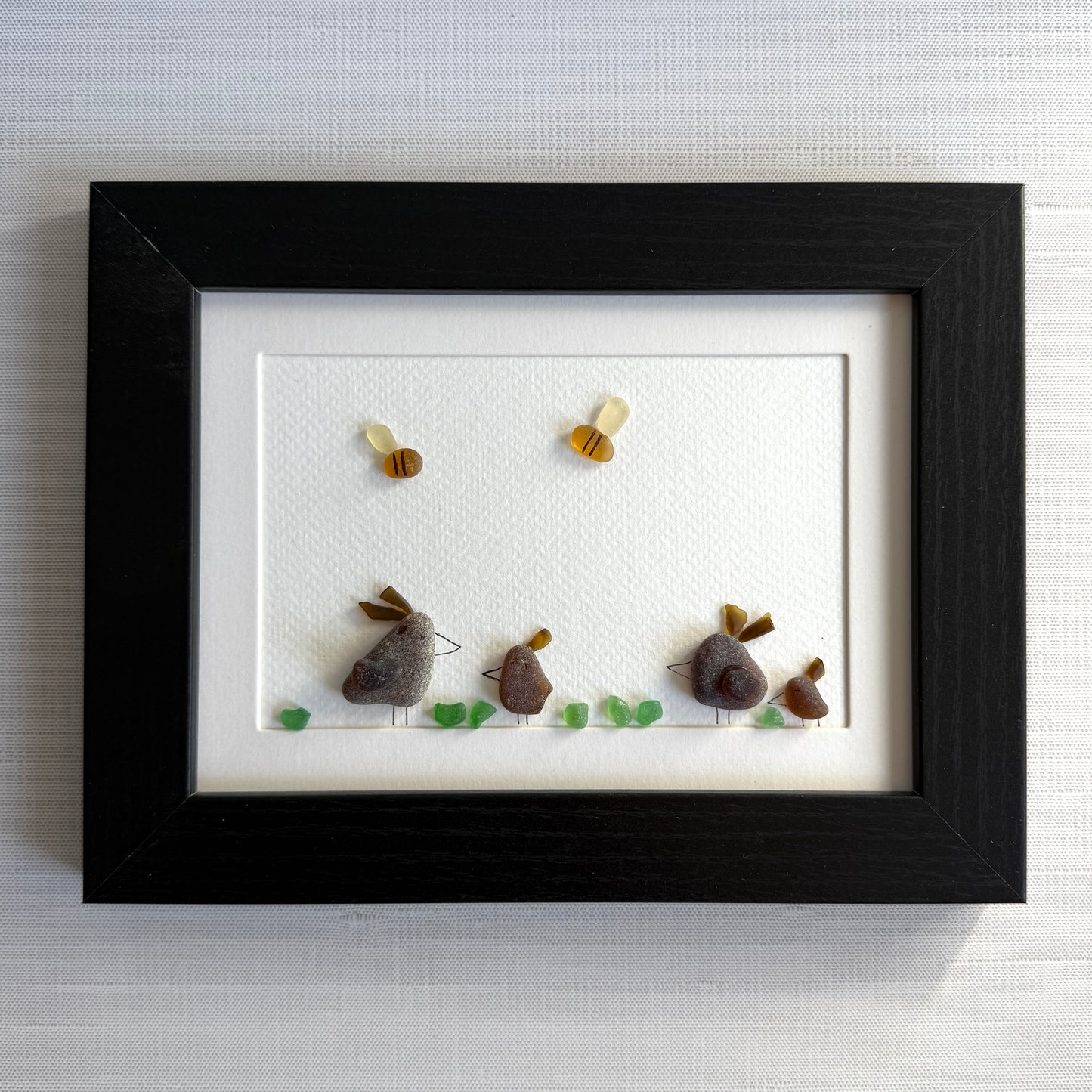 Framed sea glass artwork of hens and chickens on a white background with a black frame.