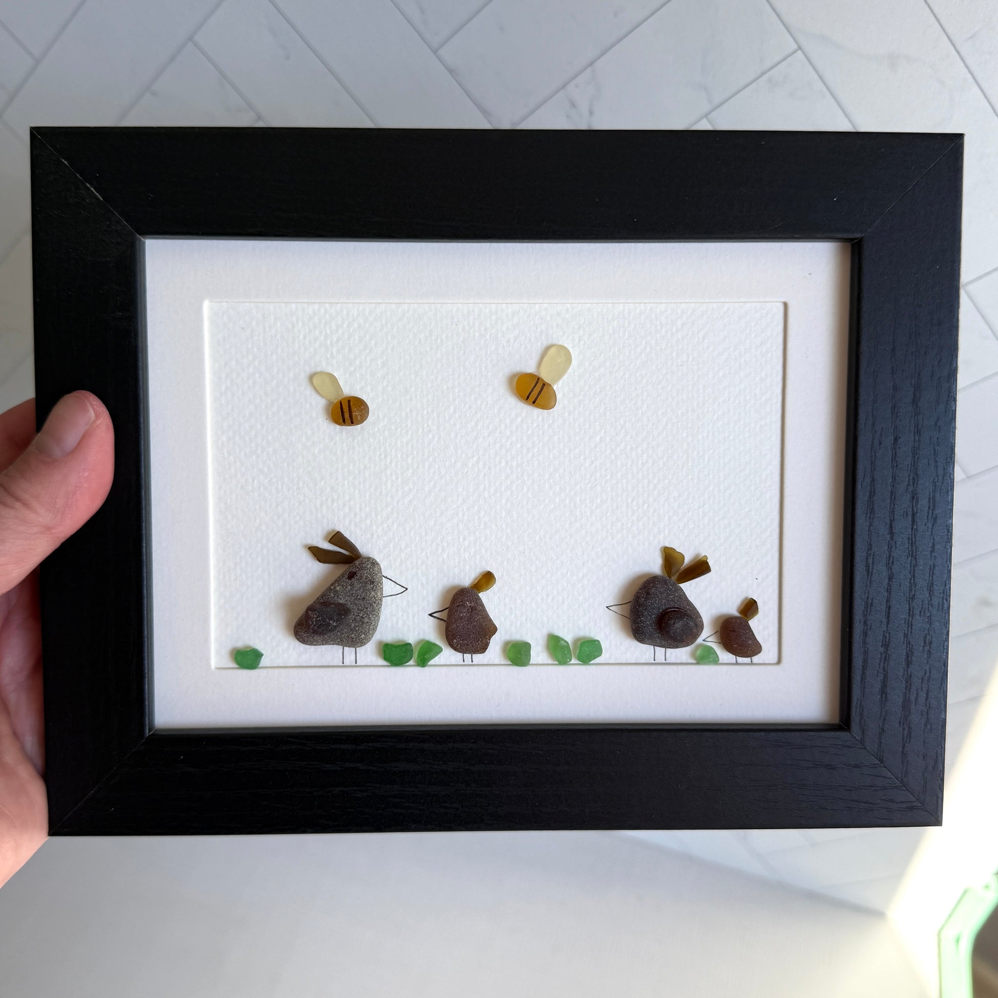 Framed sea glass artwork of hens and chickens on a white background with a black frame.