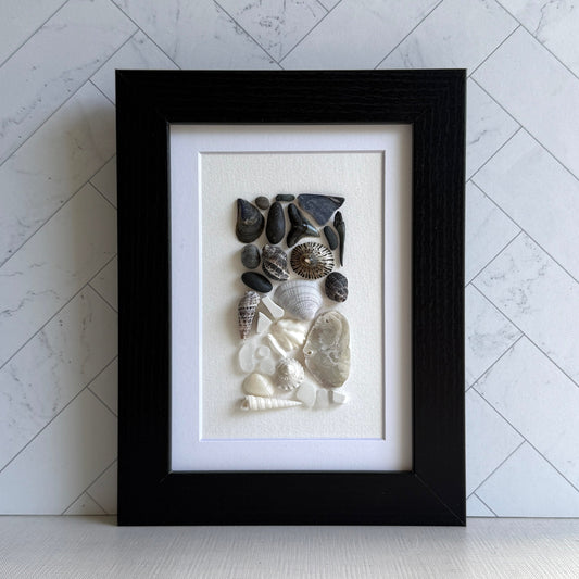 Framed artwork of pebbles, shells and sea glass on a white background