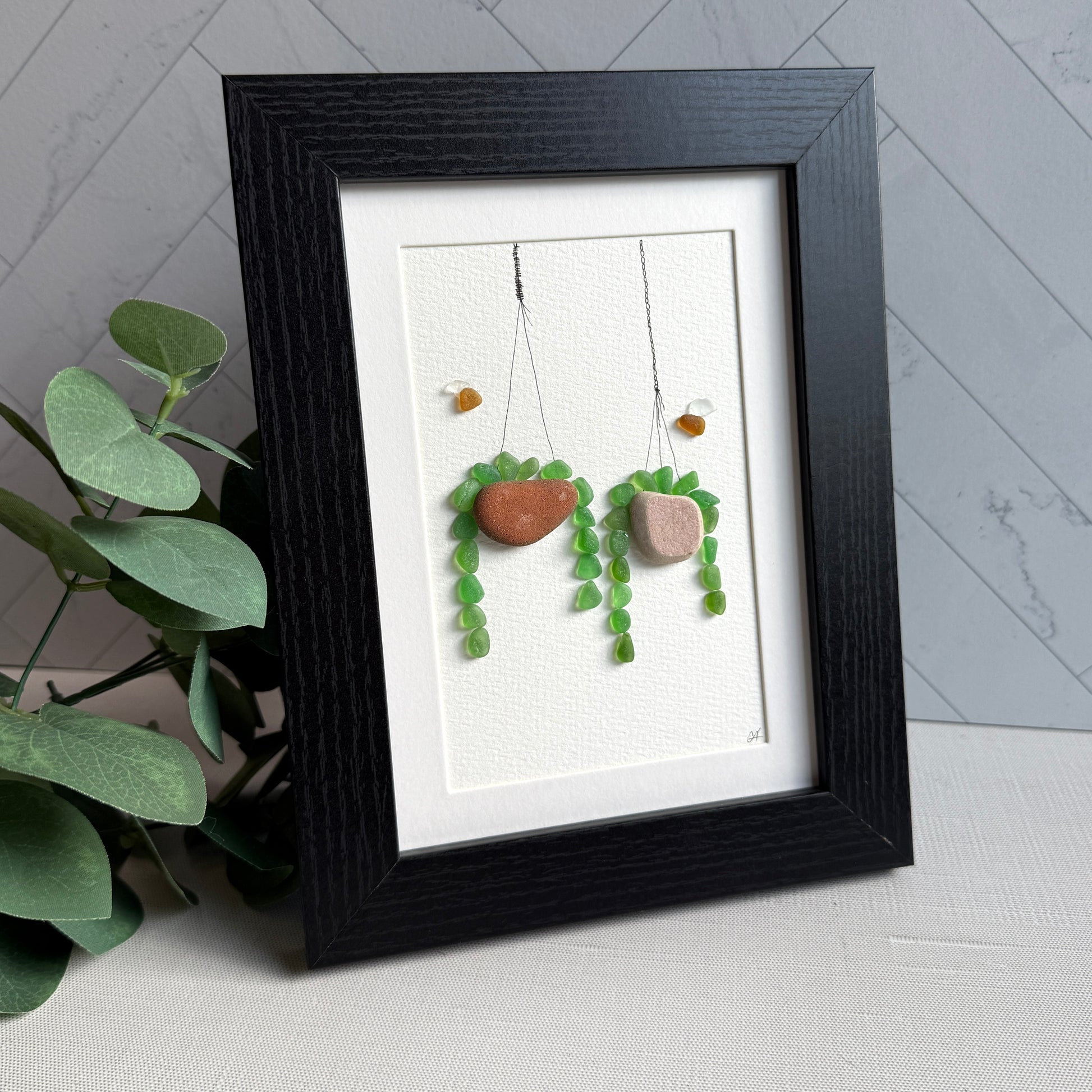 Framed sea glass artwork of hanging plants on a white background
