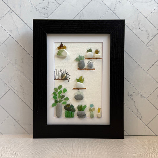 Framed 5x7 sea glass and pebble  artwork of small plants and a cat on shelves against a white background