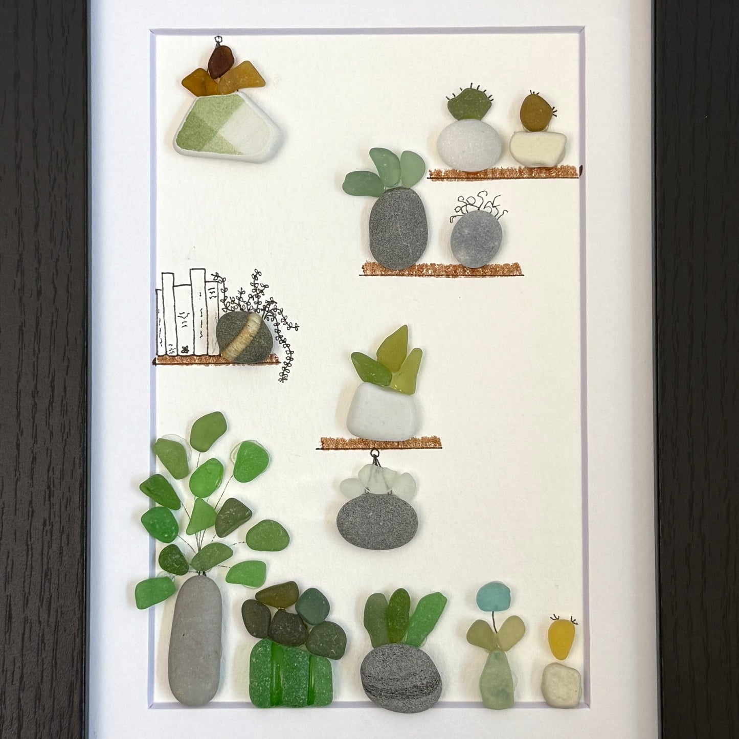Framed 5x7 sea glass and pebble  artwork of small plants and a cat on shelves against a white background