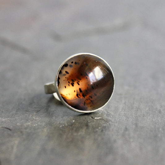 This pretty ring has a splotchy round Montana agate cabochon set in a fine and sterling silver bezel setting on a sturdy hammered band. Handmade by Will Macy in Corvallis, OR. Size 8 1/2