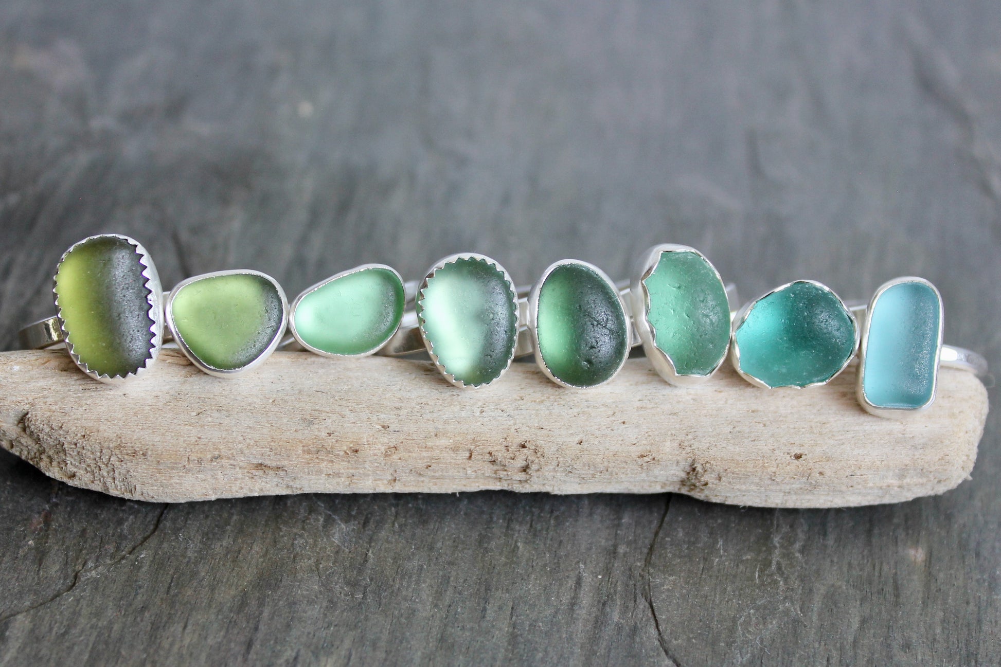 Set of sea glass rings on a piece of driftwood with a dark stone background