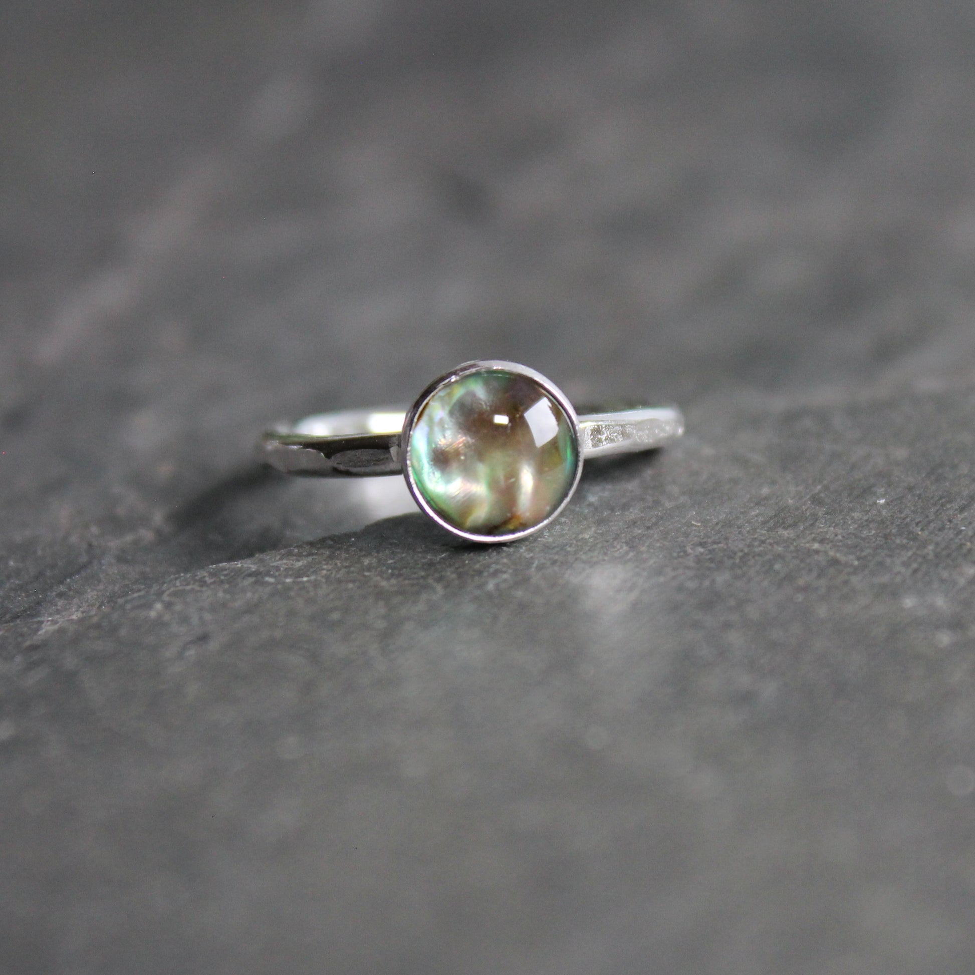 A 6mm green paua shell cabochon set in a sterling silver bezel setting on a sturdy silver hammered band. 