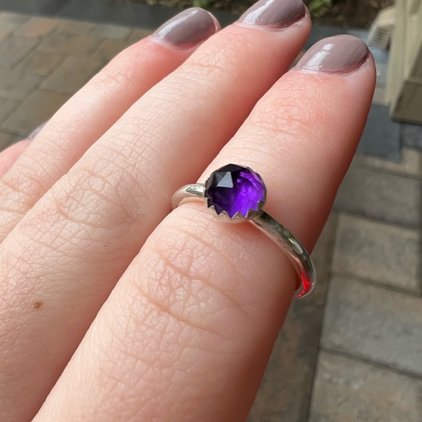 This is a 6mm rose cut round amethyst cabochon set in a sterling silver bezel setting on a sturdy silver band modeled on a hand.