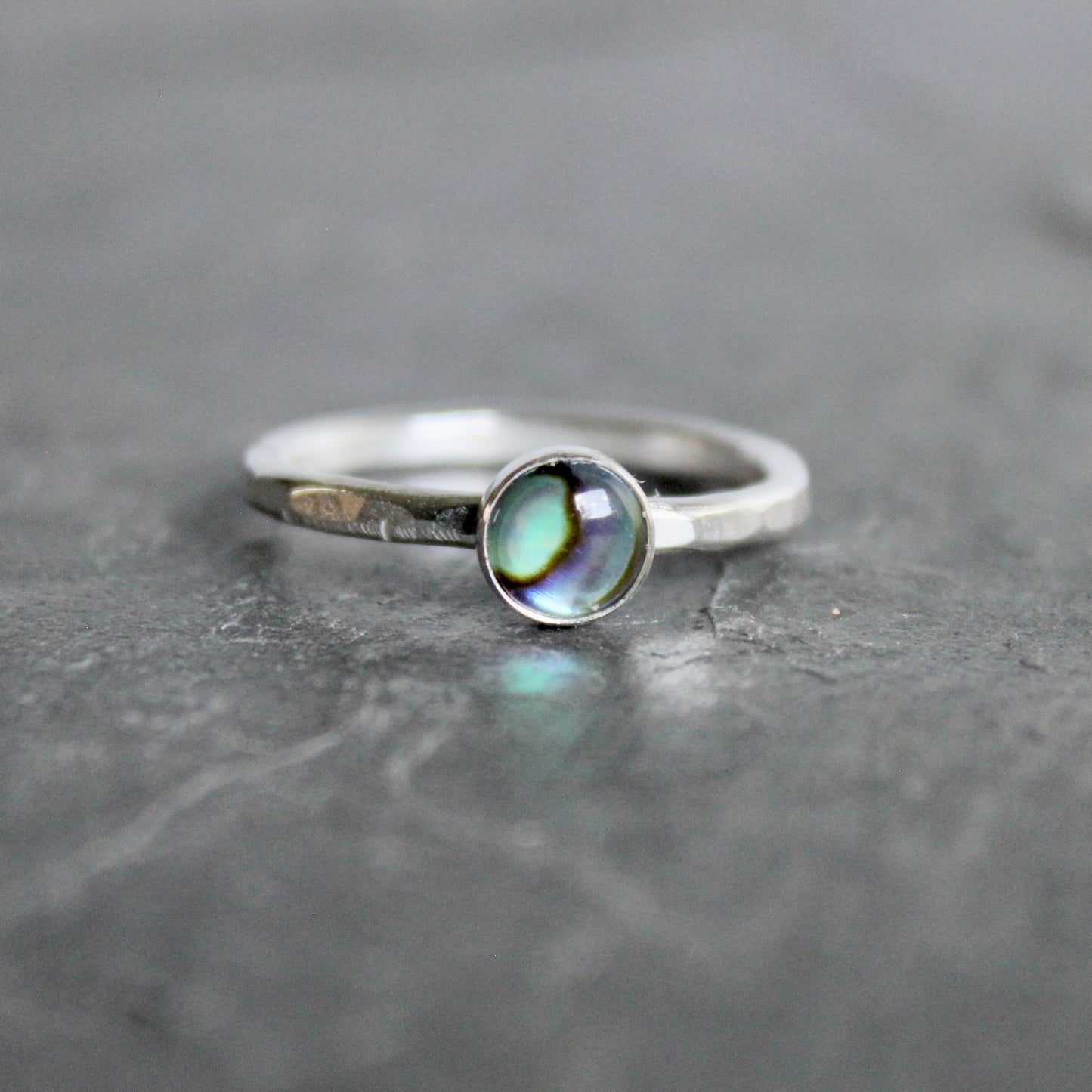 Silver ring with a green abalone cabochon on a gray surface