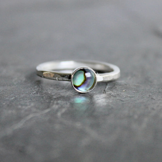 Silver ring with a green abalone cabochon on a gray surface