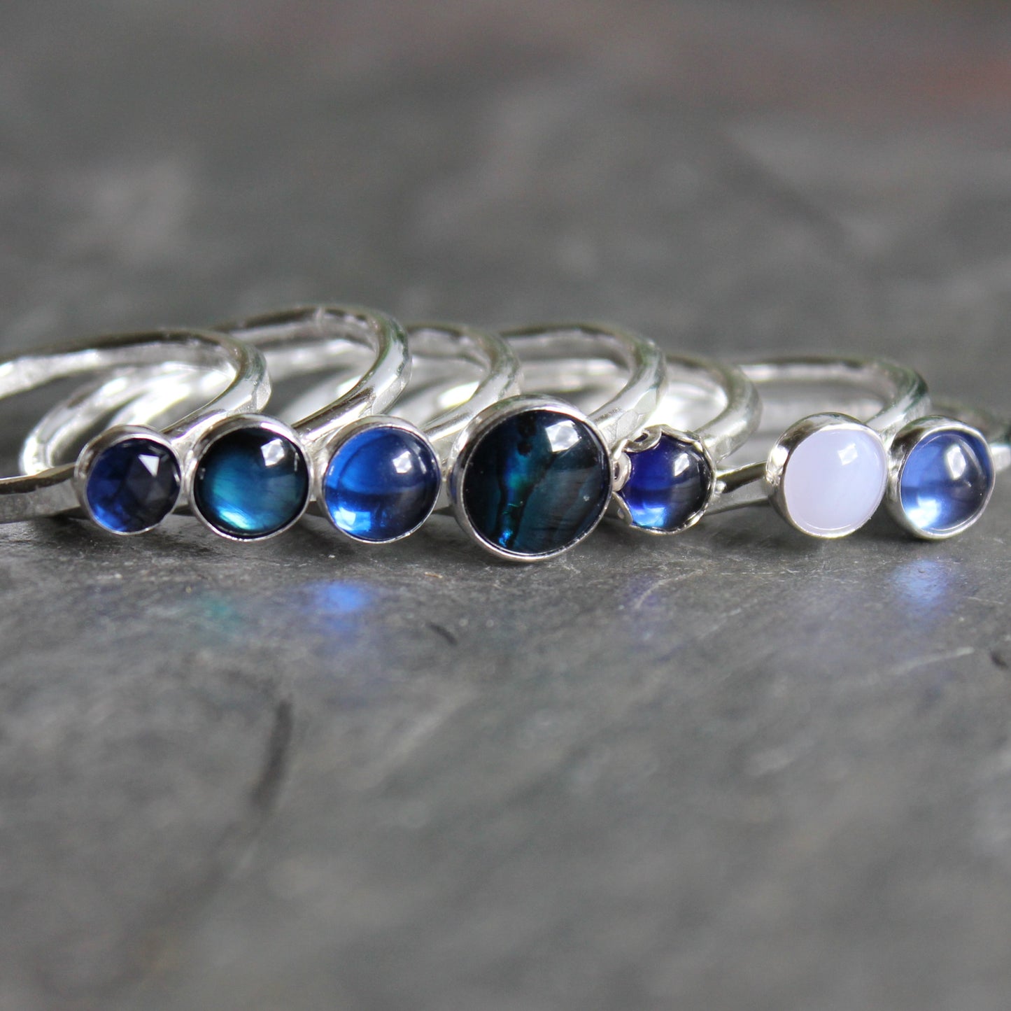 Set of silver rings with blue and white gemstones on a gray surface