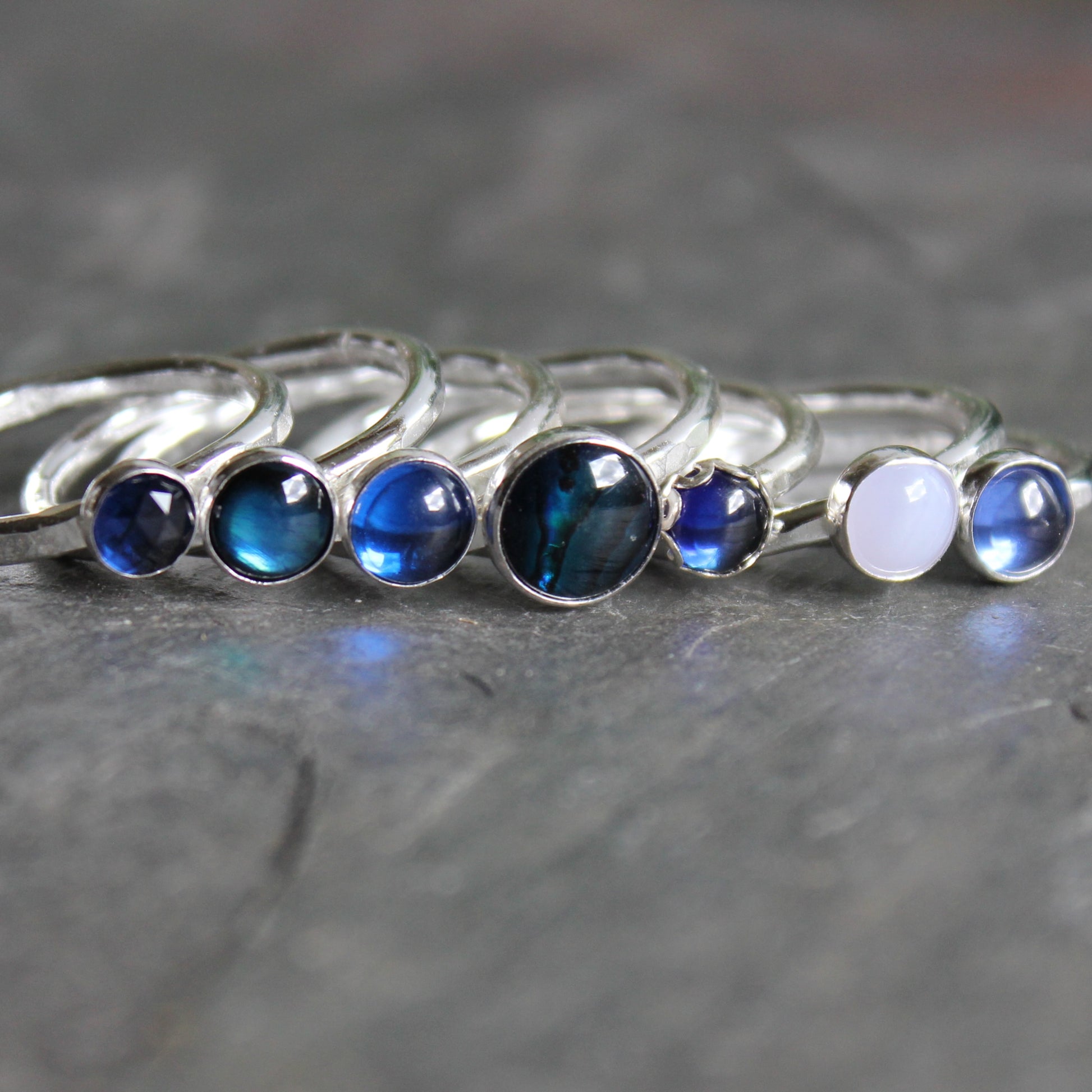 Set of silver rings with blue and white gemstones on a gray surface