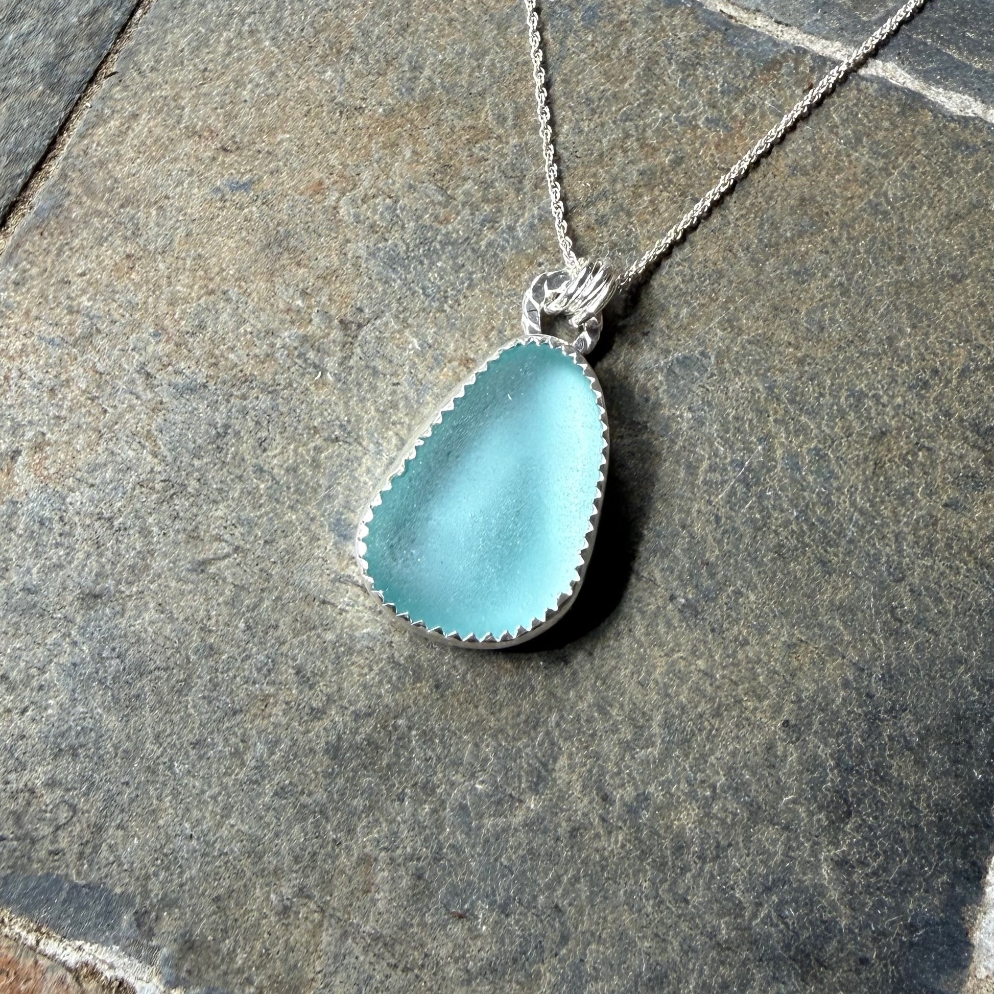 Turquoise Sea Glass pendant on a silver chain lying on stone pavement