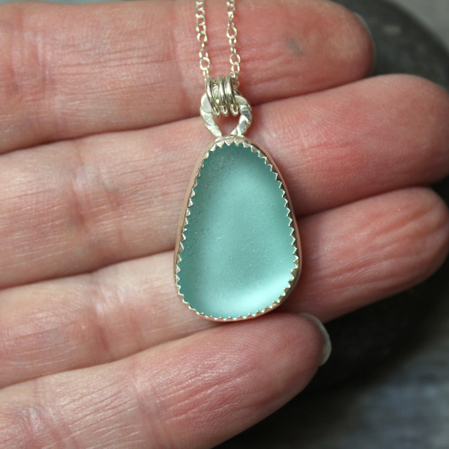 Teal Sea Glass necklace held between fingers