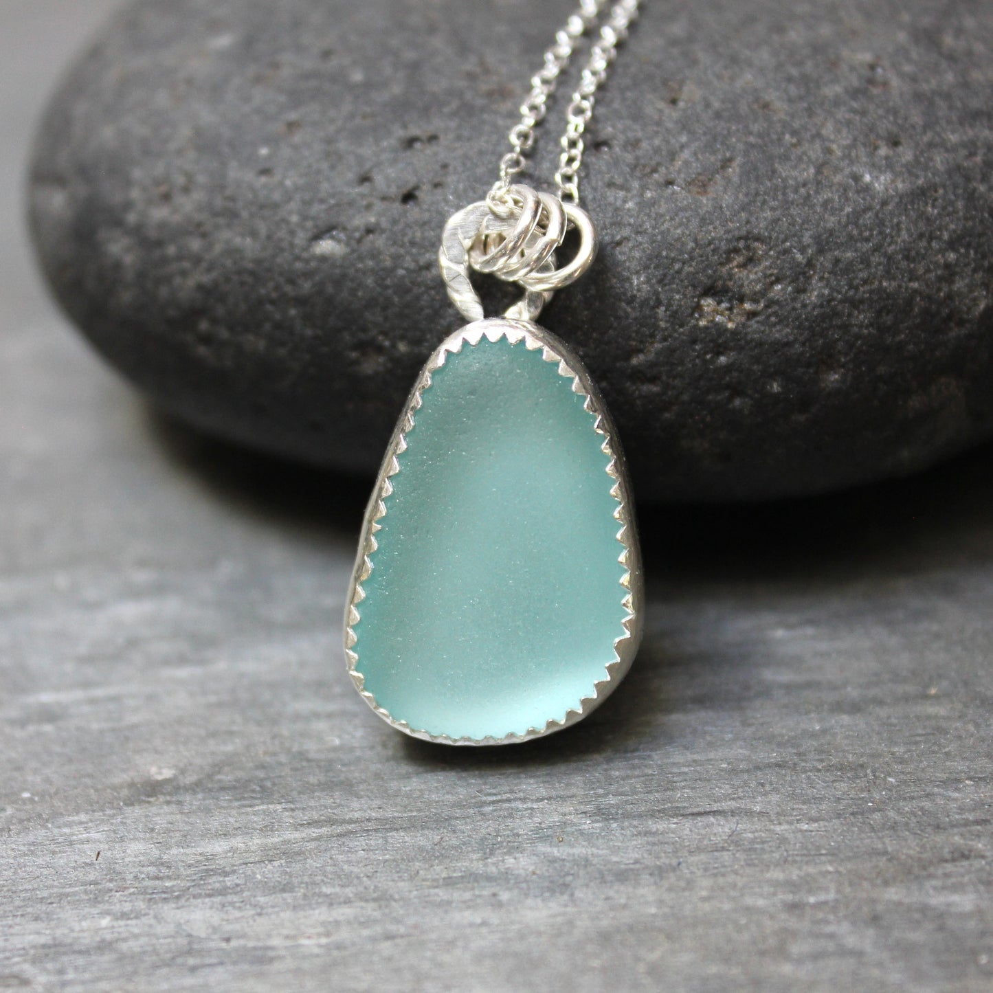 Teal sea glass pendant on a silver chain against a stone background