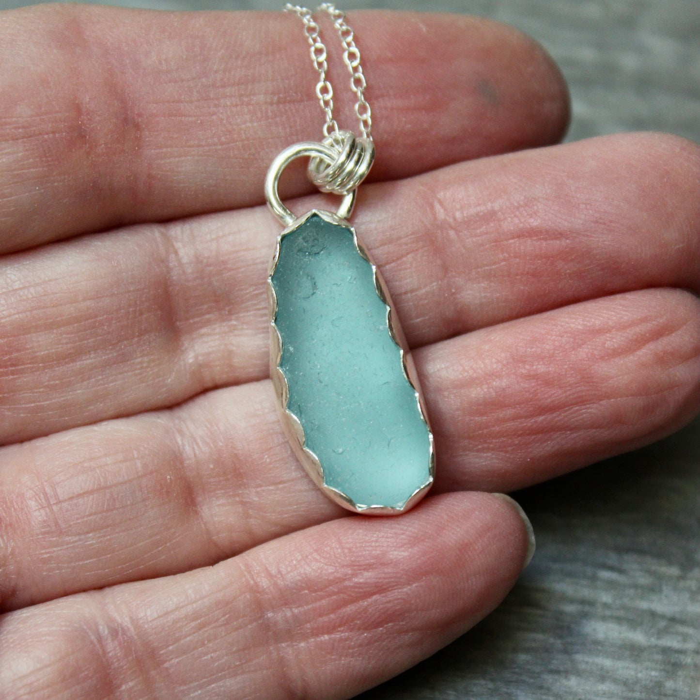 Turquoise sea glass necklace held in a hand against a neutral background