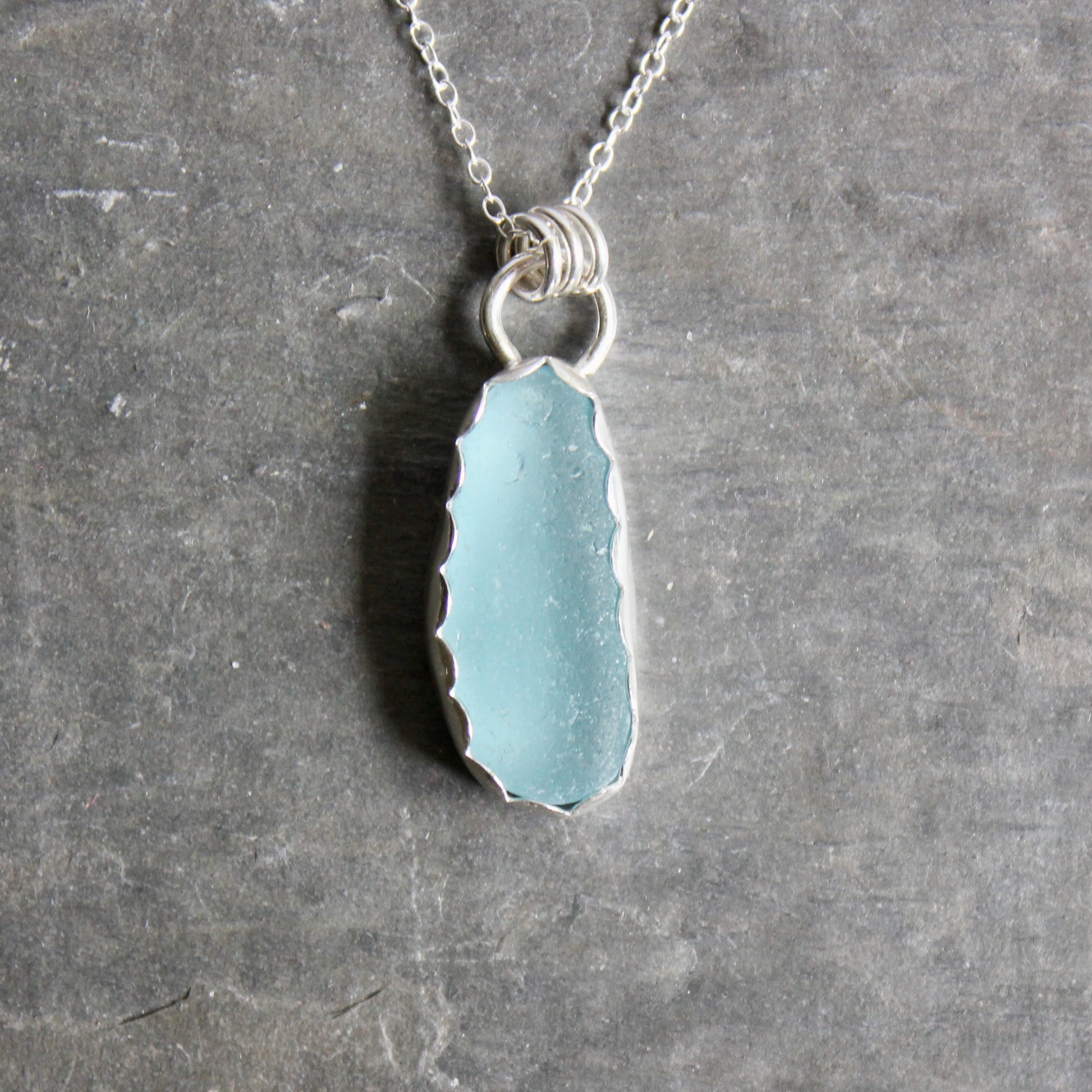 Necklace with a light blue sea glass on a gray surface