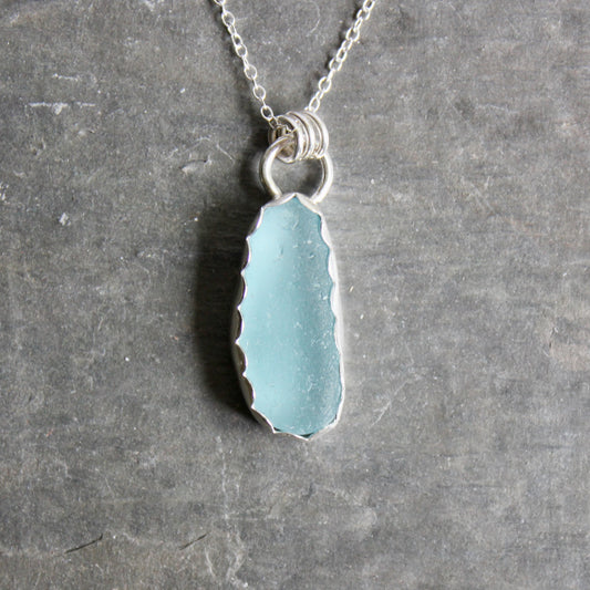 Necklace with a light blue sea glass on a gray surface