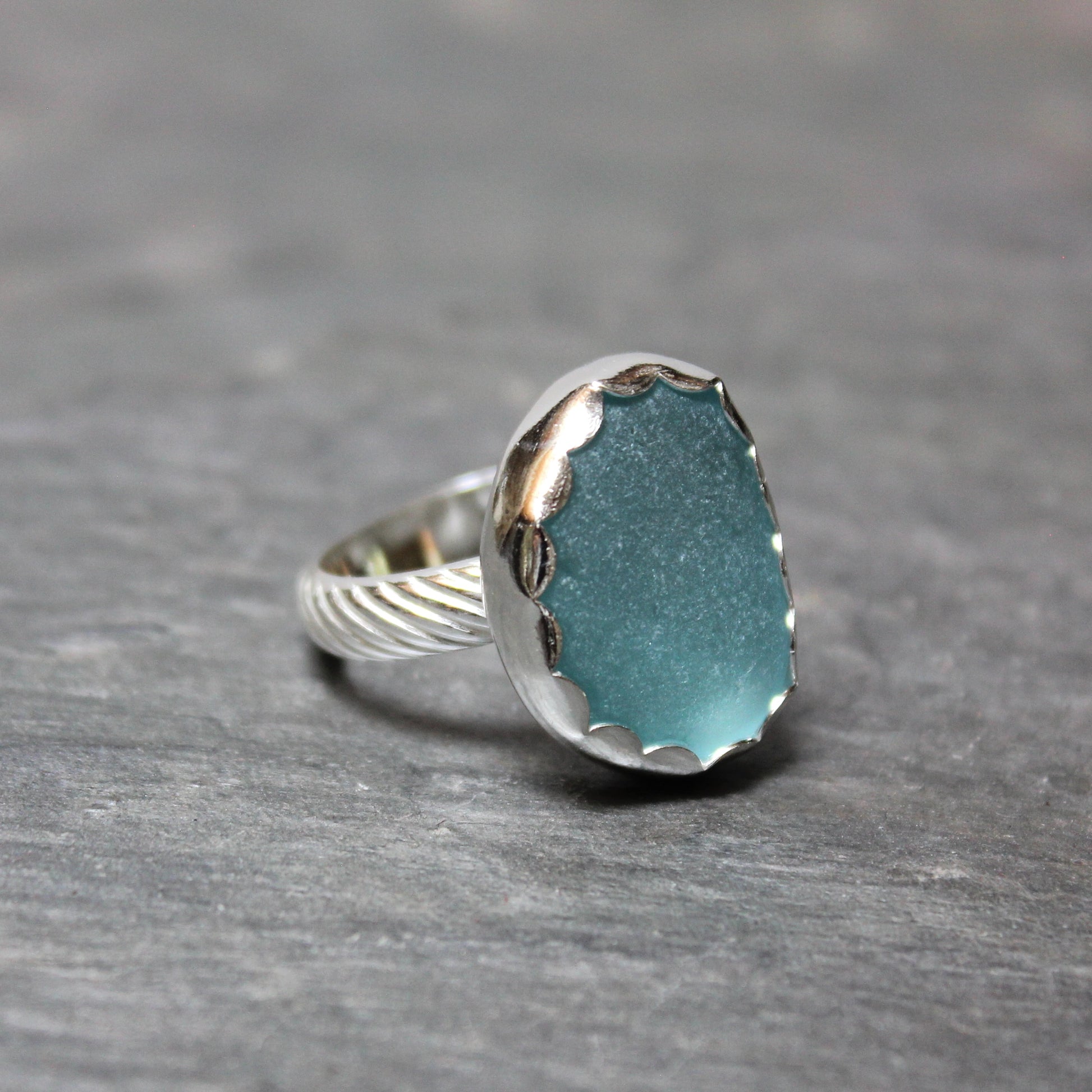 Aqua Sea Glass ring with silver band on a gray background