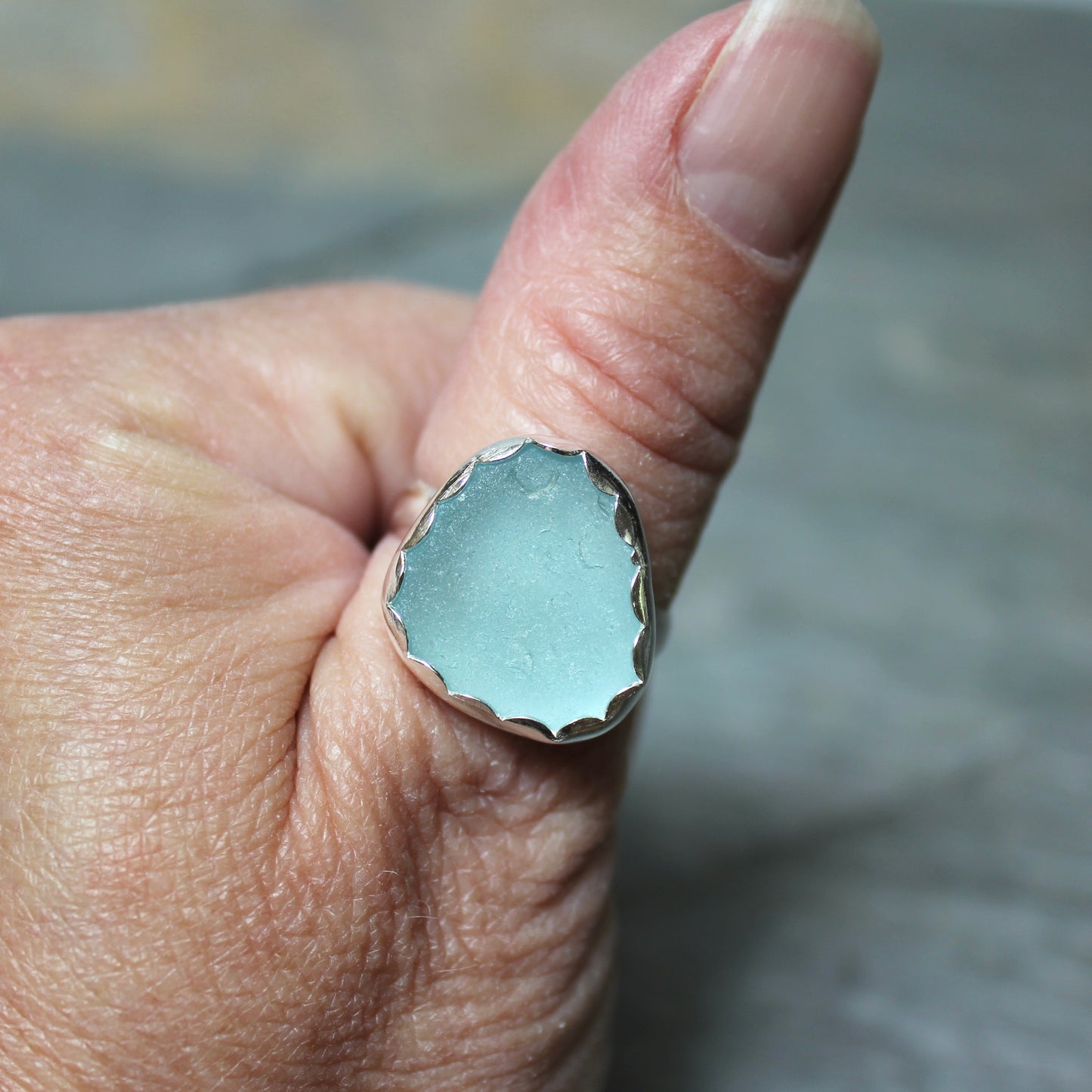 Hand wearing a ring with light blue sea glass on a blurred background
