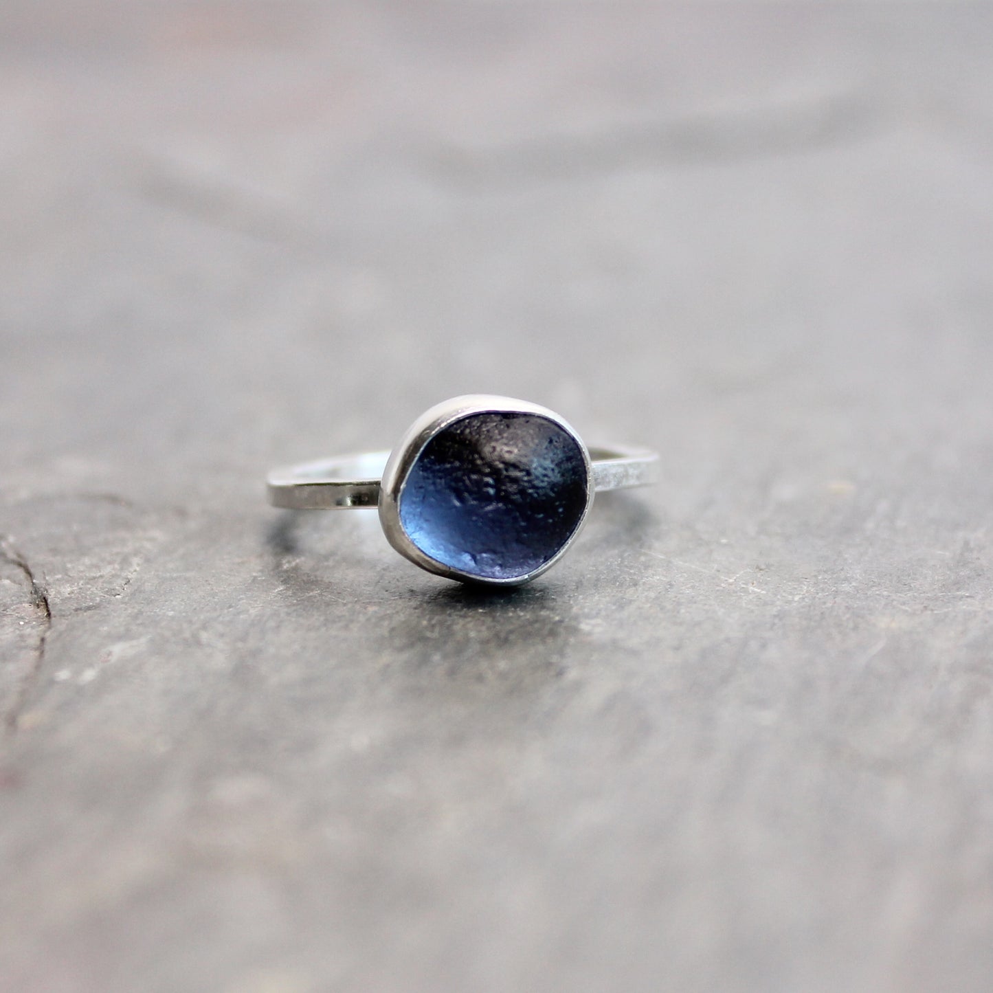 Silver ring with blue sea glass on a gray surface