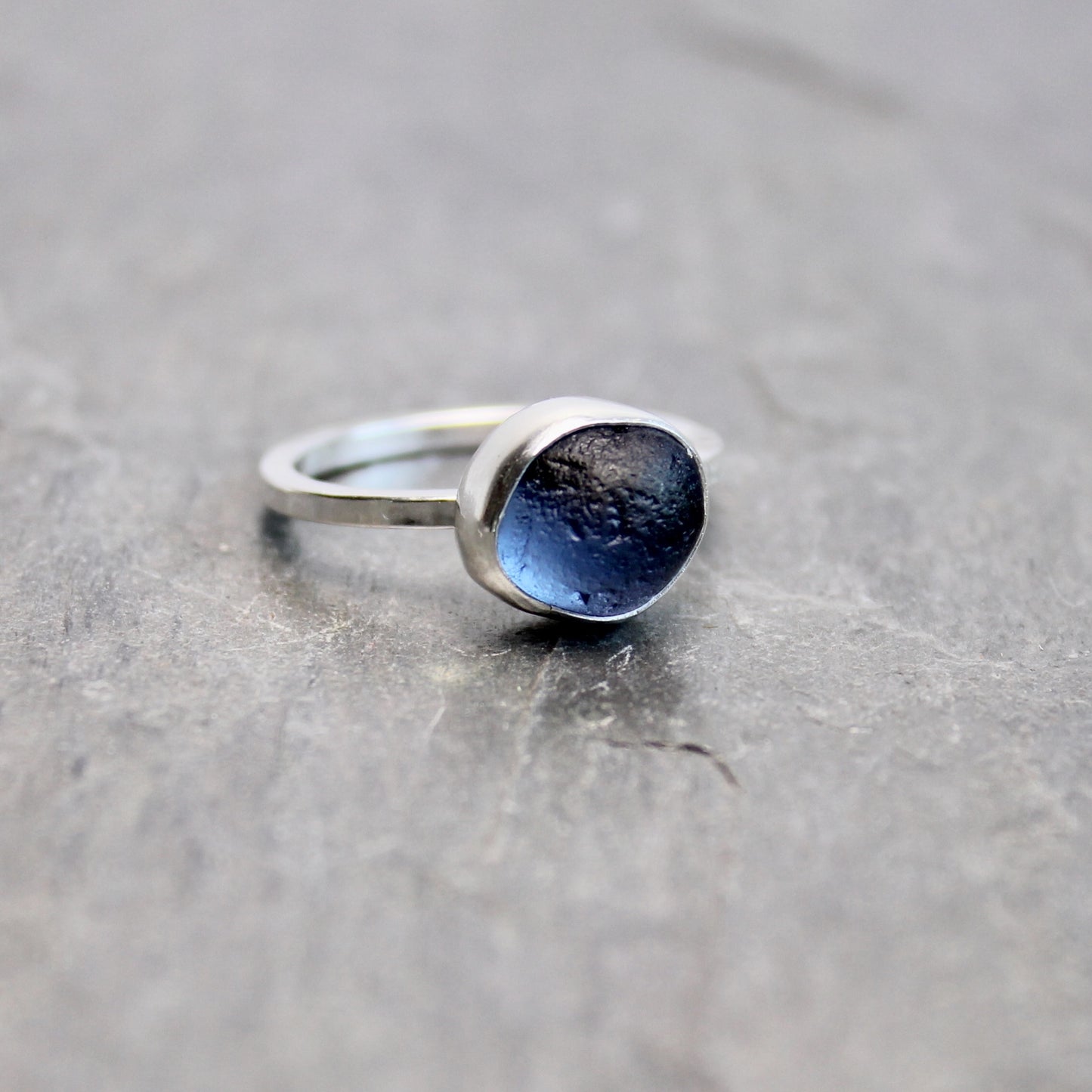 Silver ring with blue sea glass on a gray surface