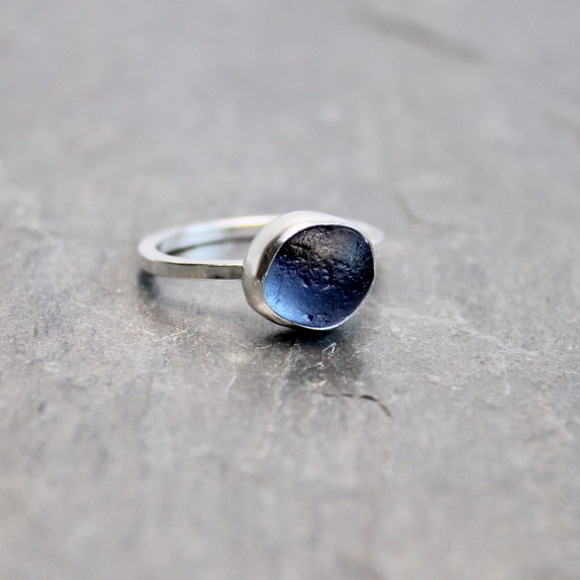Silver ring with blue sea glass on a gray surface
