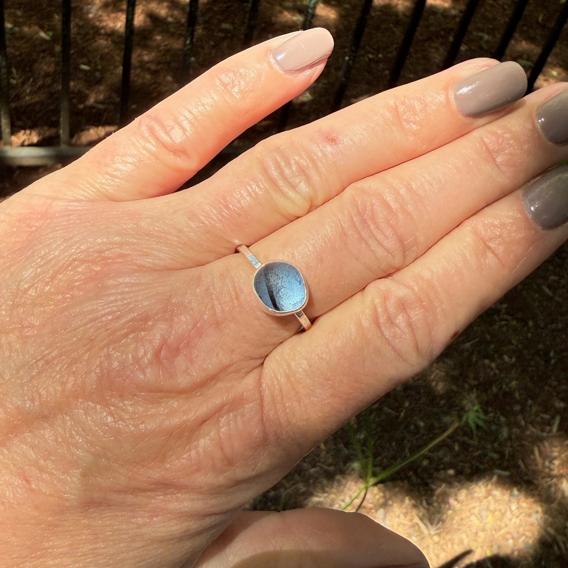 Hand wearing a ring with blue sea glass outdoors