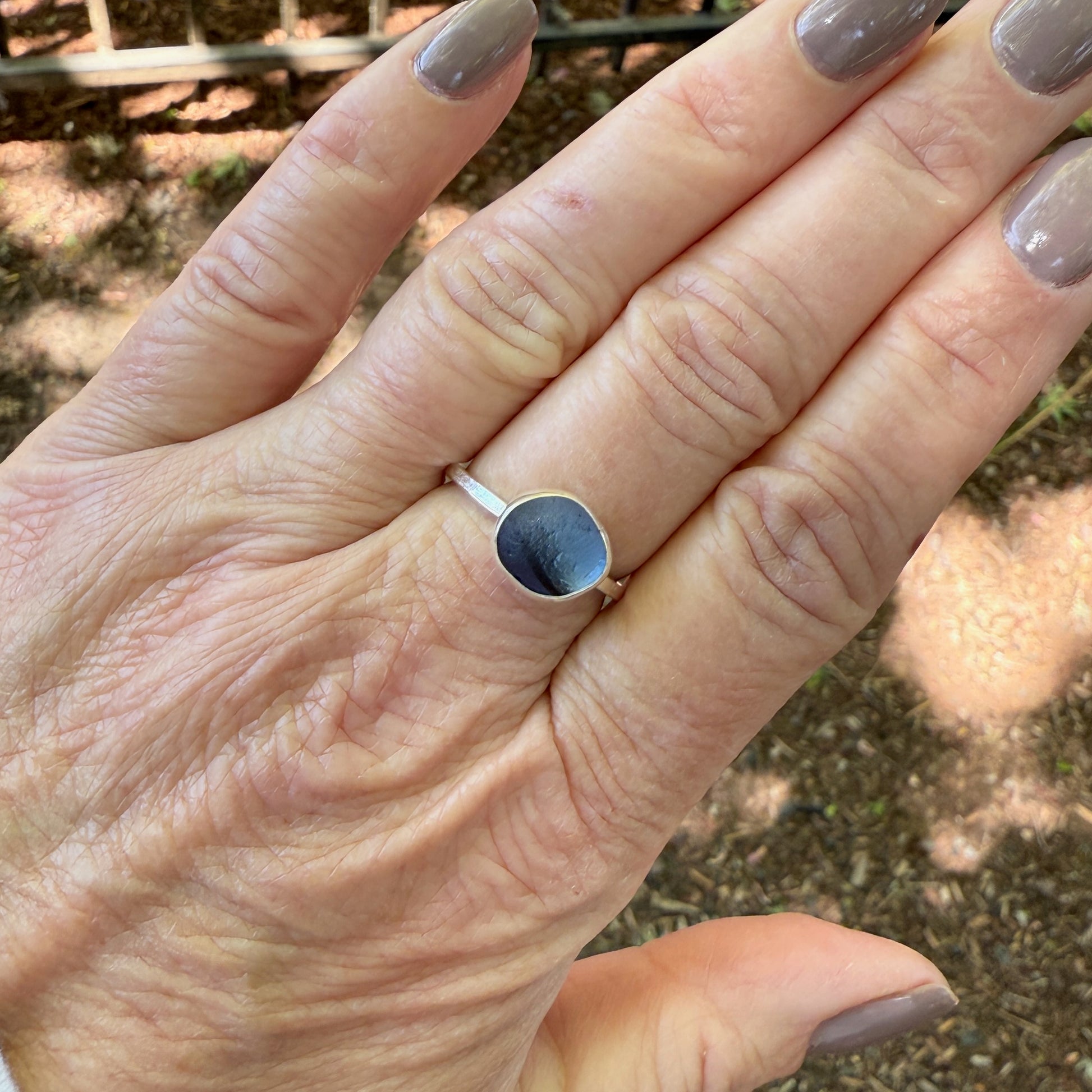 Hand wearing a silver ring with blue sea glass against a natural background