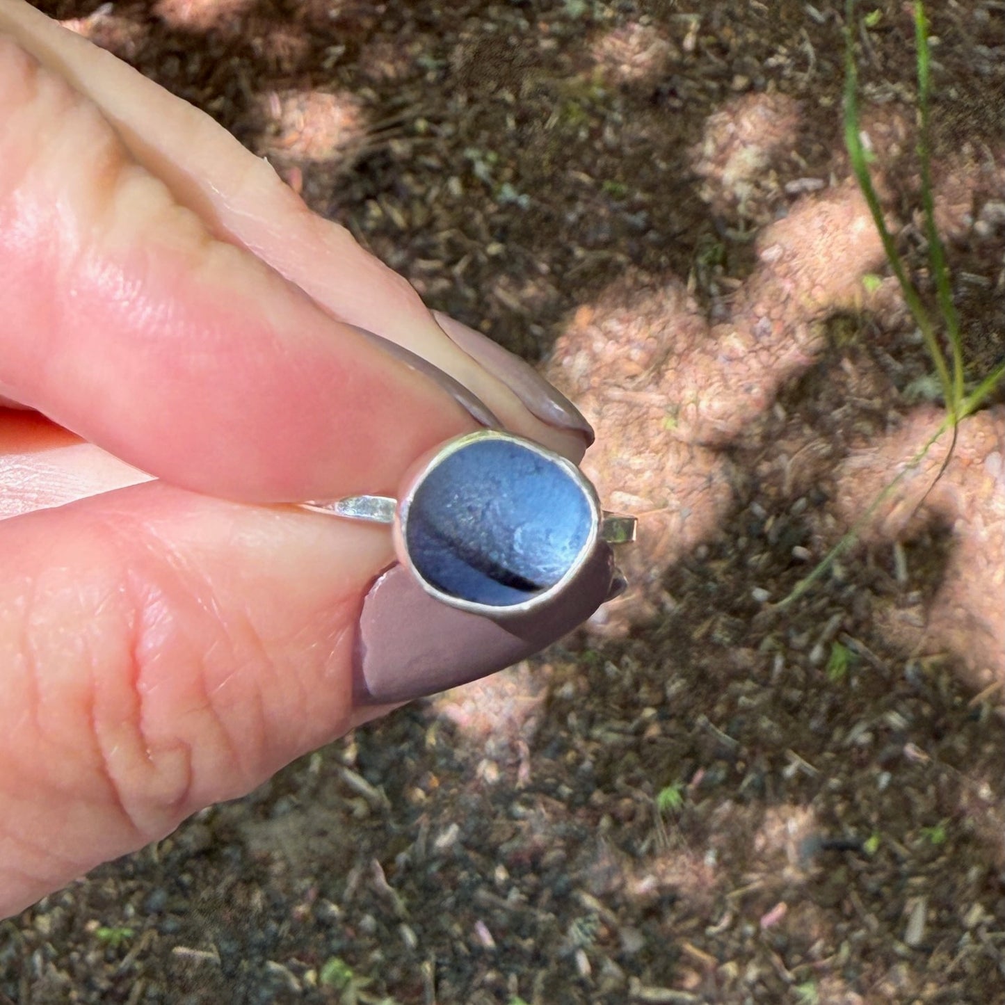 Hand wearing a silver ring with a blue sea glass against a natural background