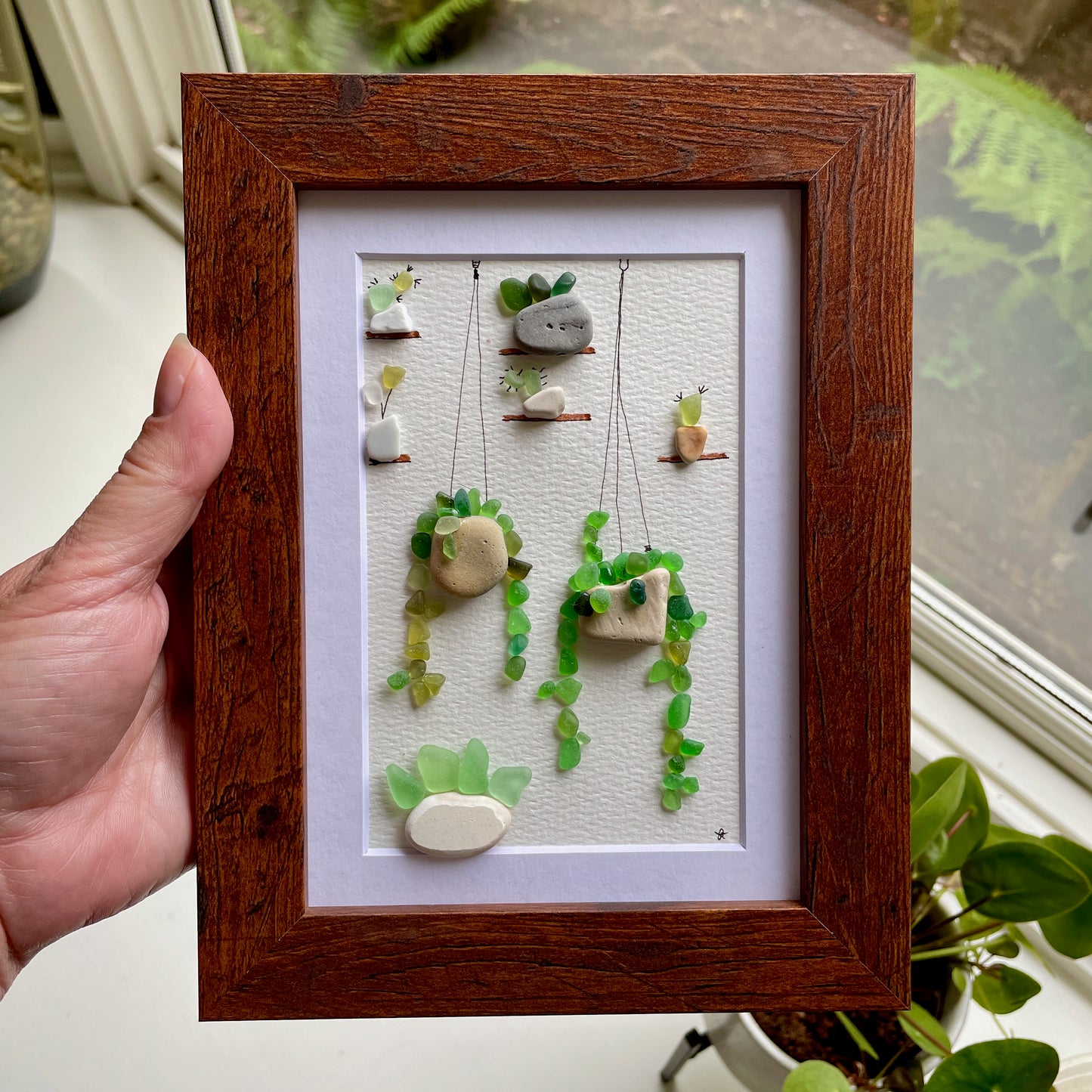 This is a framed 5 x 7 inch sea glass art picture featuring several potted succulents, cactus and plants made with sea glass and beach pottery. This item is perfect for gift giving and ready to hang or place on a shelf.  