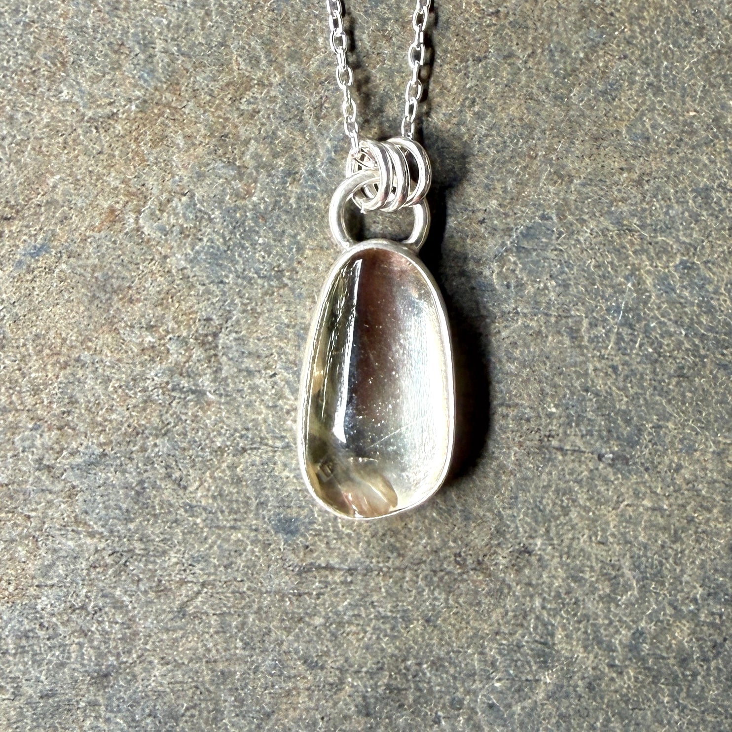 Silver pendant necklace with a champagne clear sunstone on a stone surface