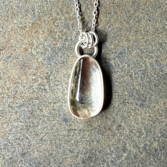 Silver pendant necklace with a champagne clear sunstone on a stone surface