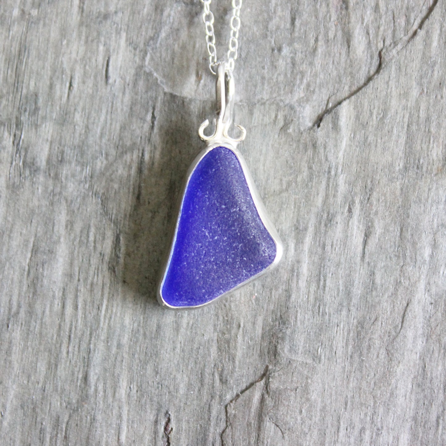 Cobalt sea glass pendant on a silver chain against a wooden background