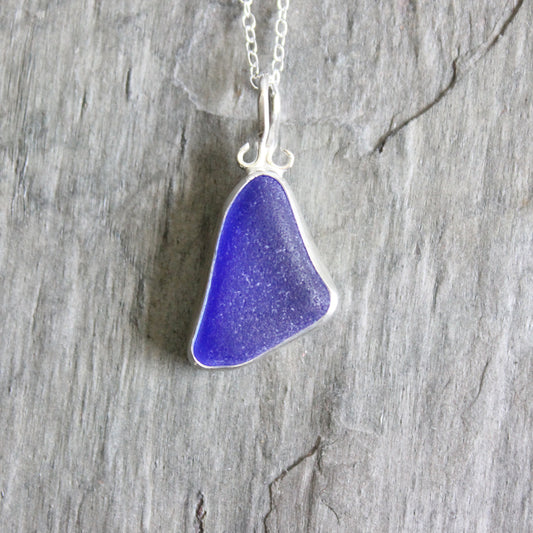 Cobalt sea glass pendant on a silver chain against a wooden background
