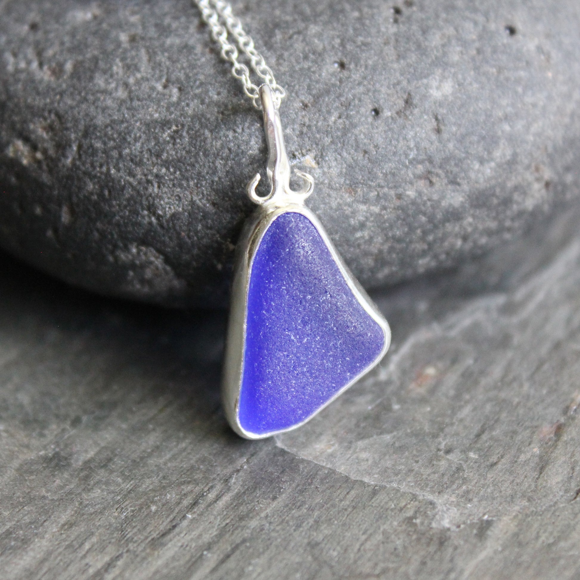 Blue sea glass pendant on a silver chain against a stone background