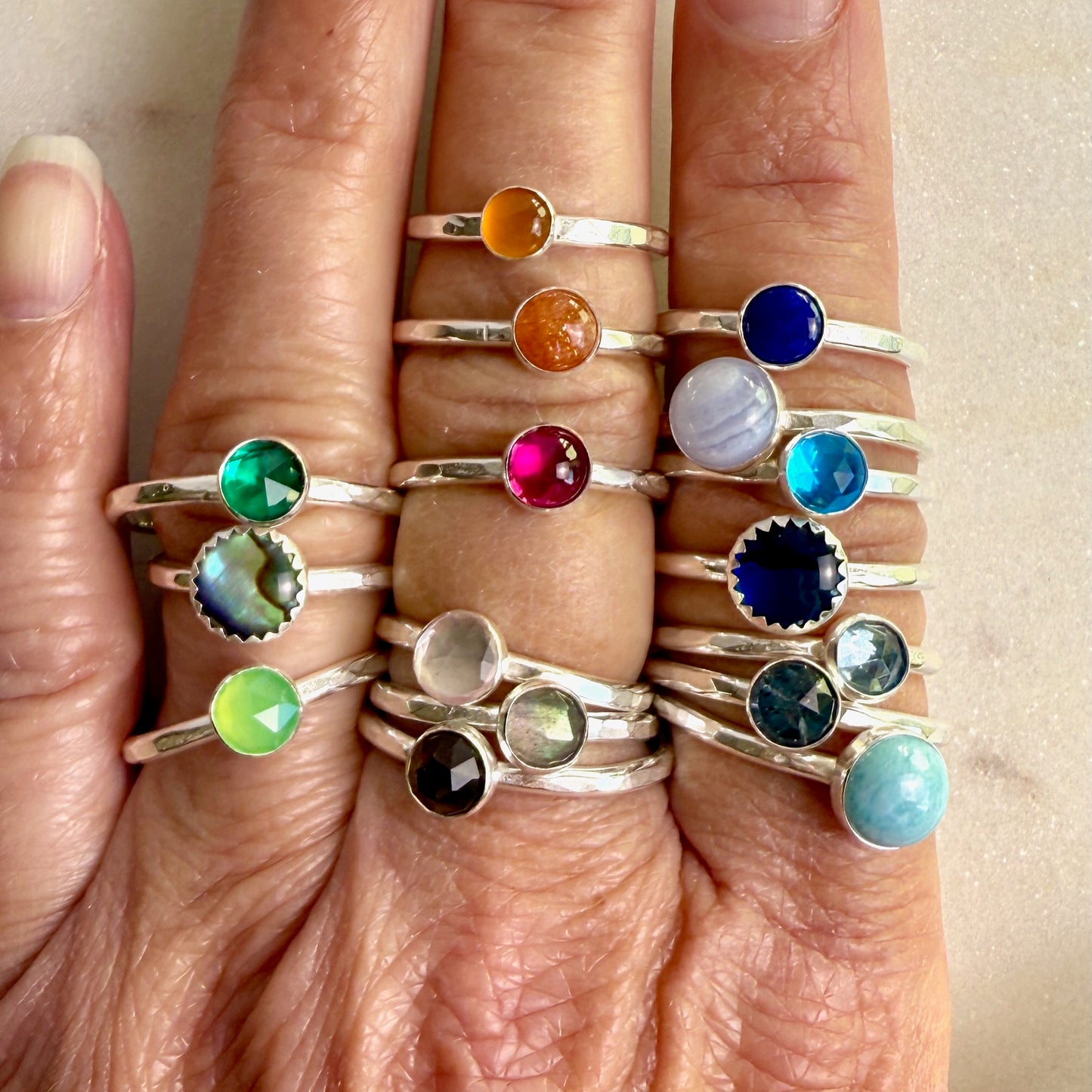 Close-up of fingers wearing multiple rings with colorful gemstones on a neutral background