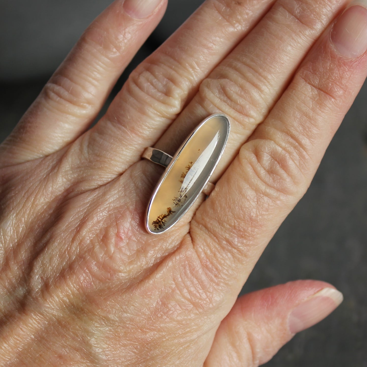 Close-up of a hand wearing a silver ring with a natural stone on a blurred background