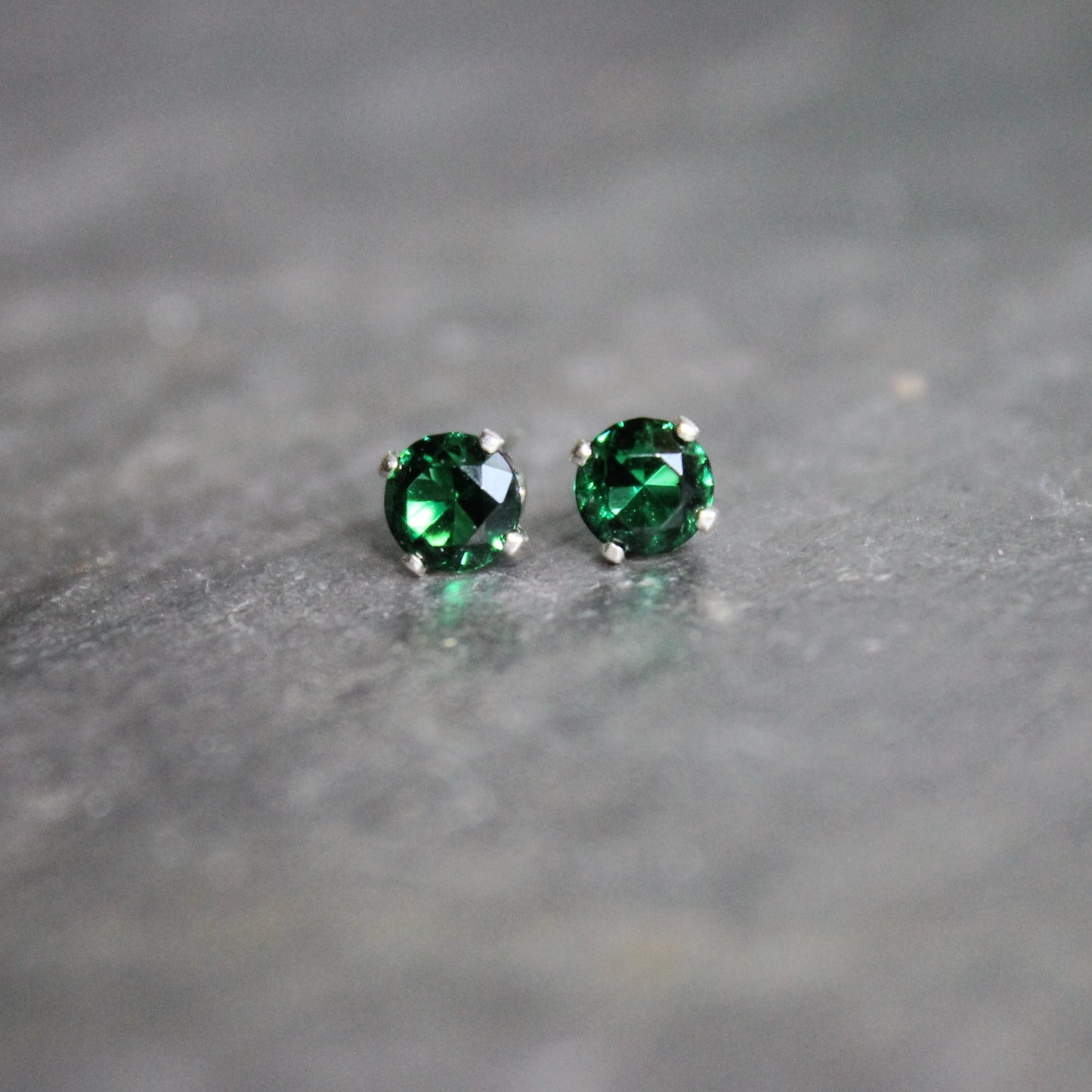 These stud earrings have 4mm round faceted lab created emeralds set in sterling silver 4-prong stud earring settings with earring backs. 