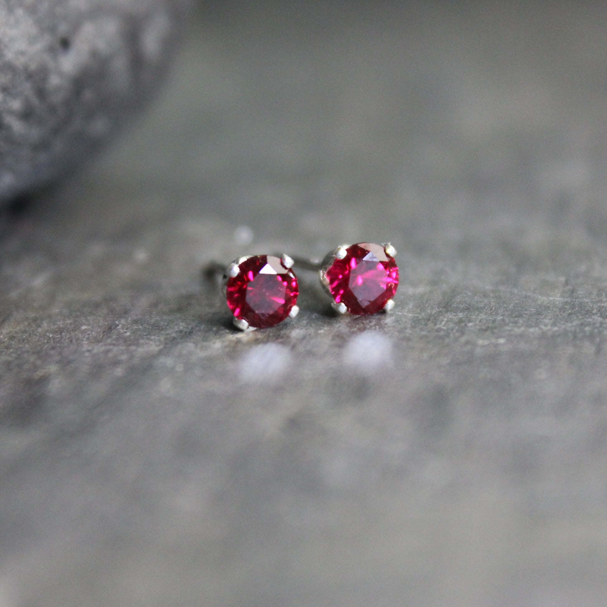 These stud earrings have 4mm round lab created faceted garnets set in sterling silver 4-prong earring settings with ear nuts. 