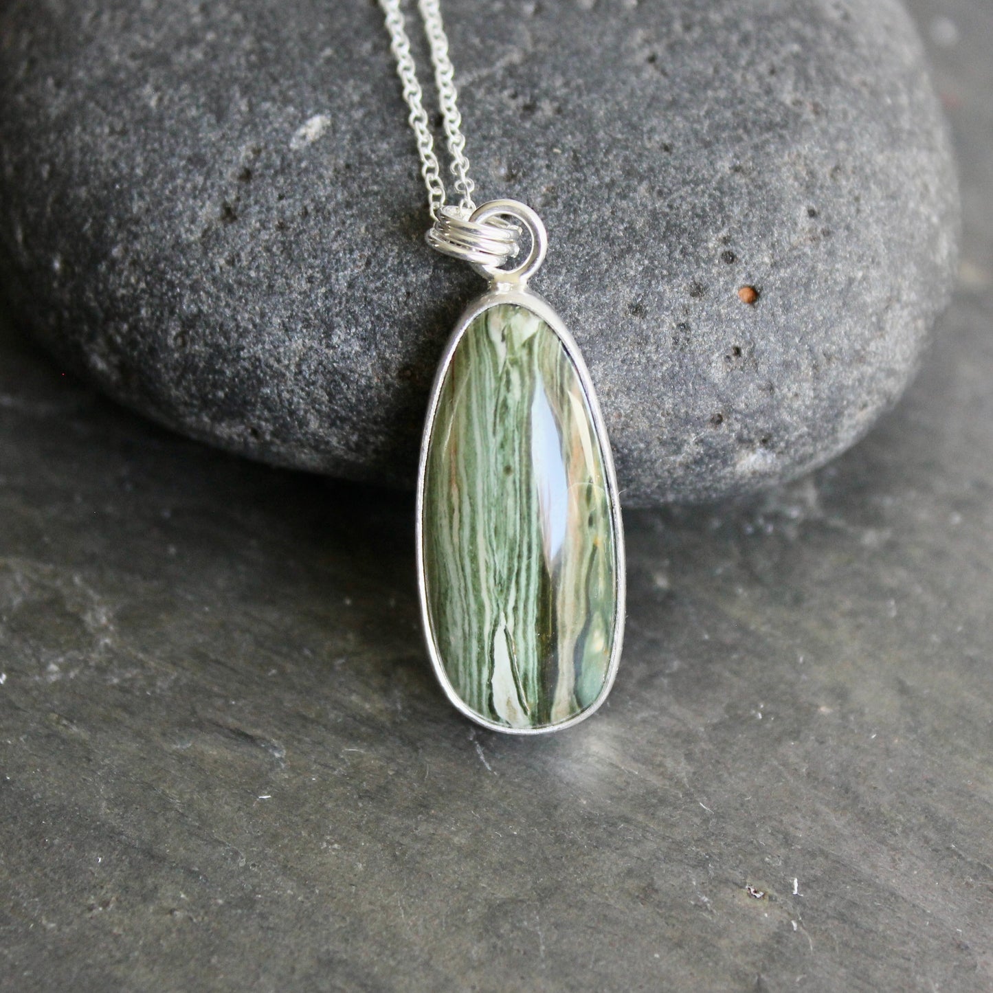 Green stone pendant on a silver chain against a gray stone background