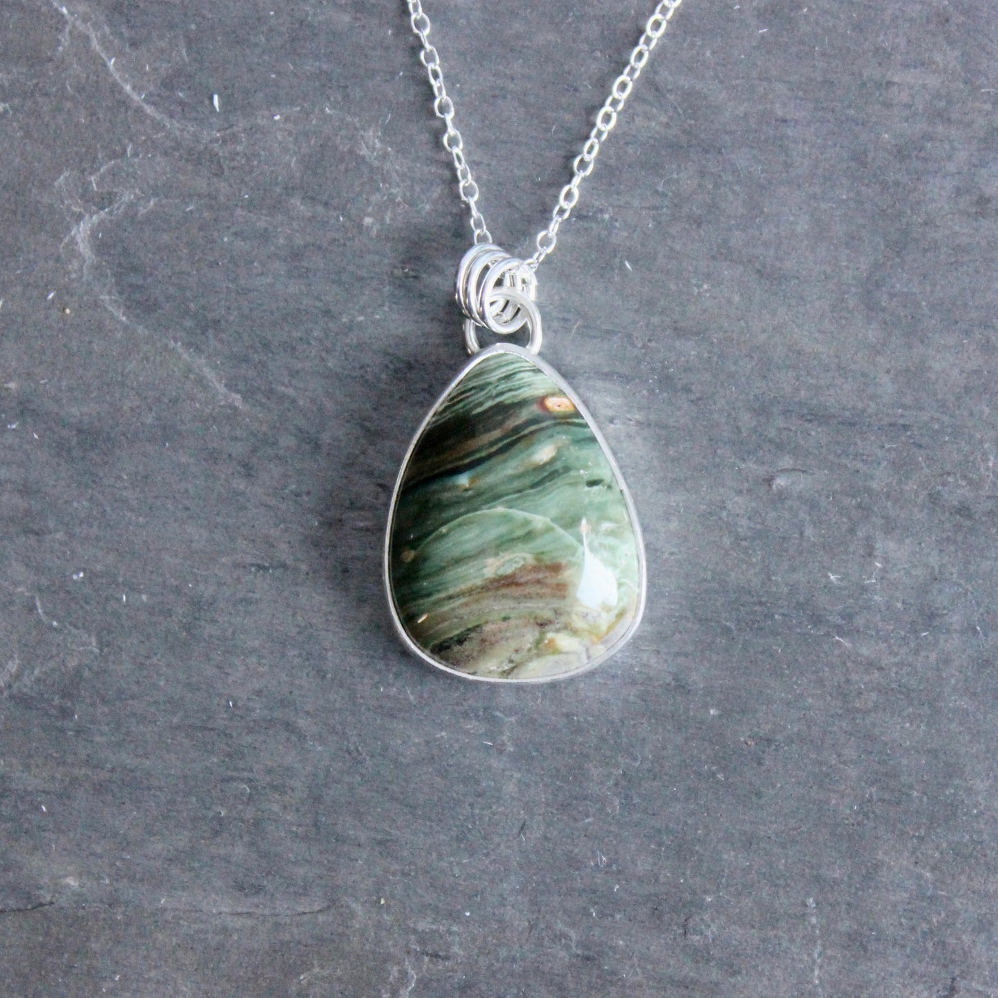 Teardrop-shaped pendant with a bezel set gary green jasper on a chain against a gray background