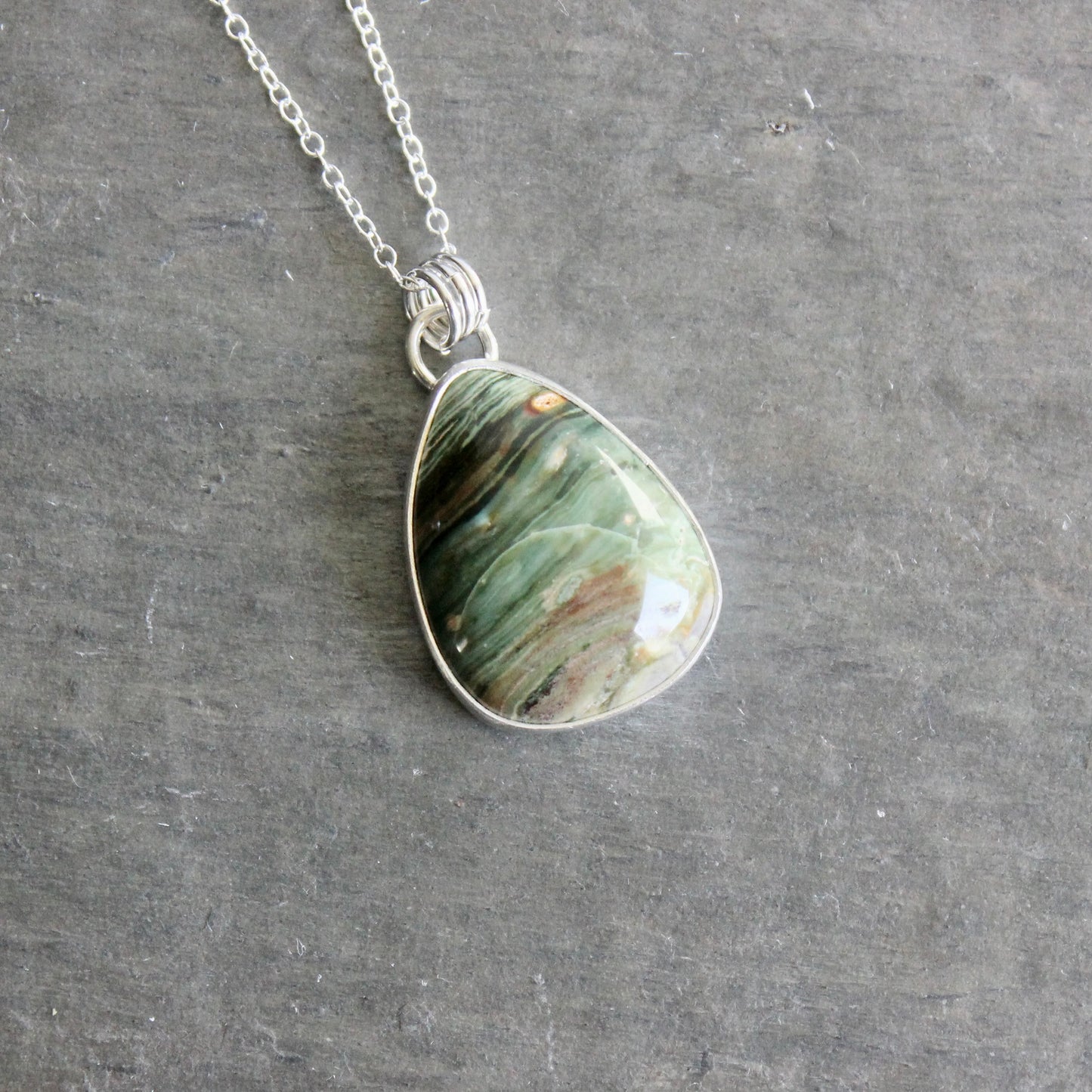 Teardrop-shaped pendant with a bezel set gary green jasper on a chain against a gray background