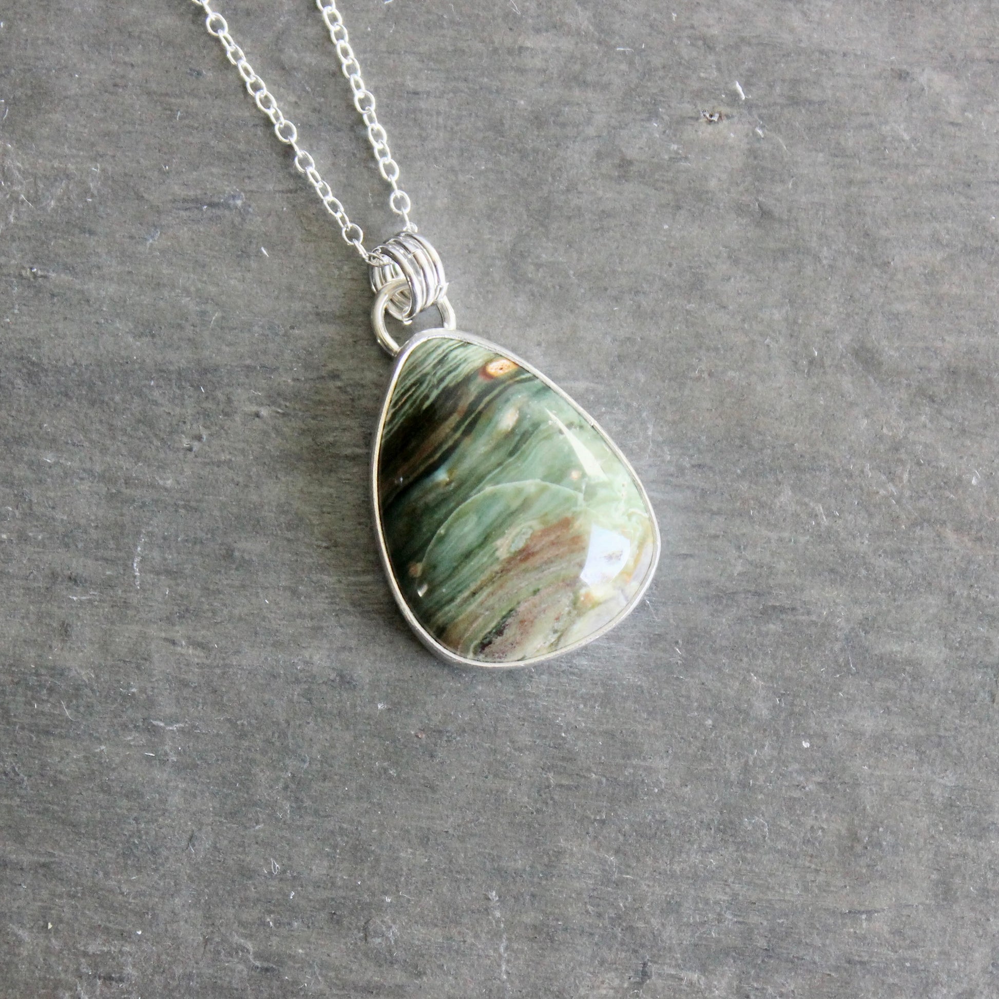 Teardrop-shaped pendant with a bezel set gary green jasper on a chain against a gray background