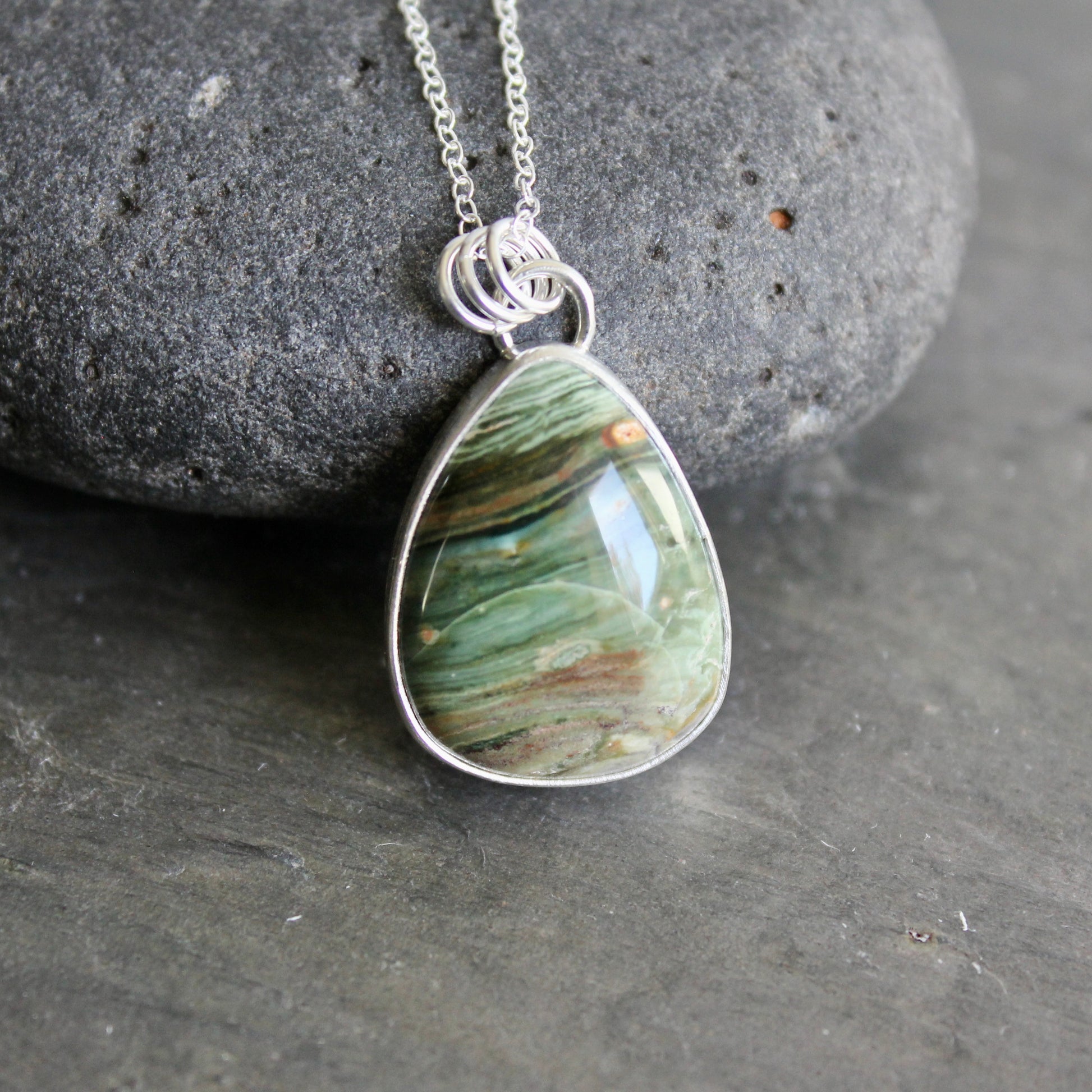 Teardrop-shaped pendant with a bezel set gary green jasper on a chain against a gray background