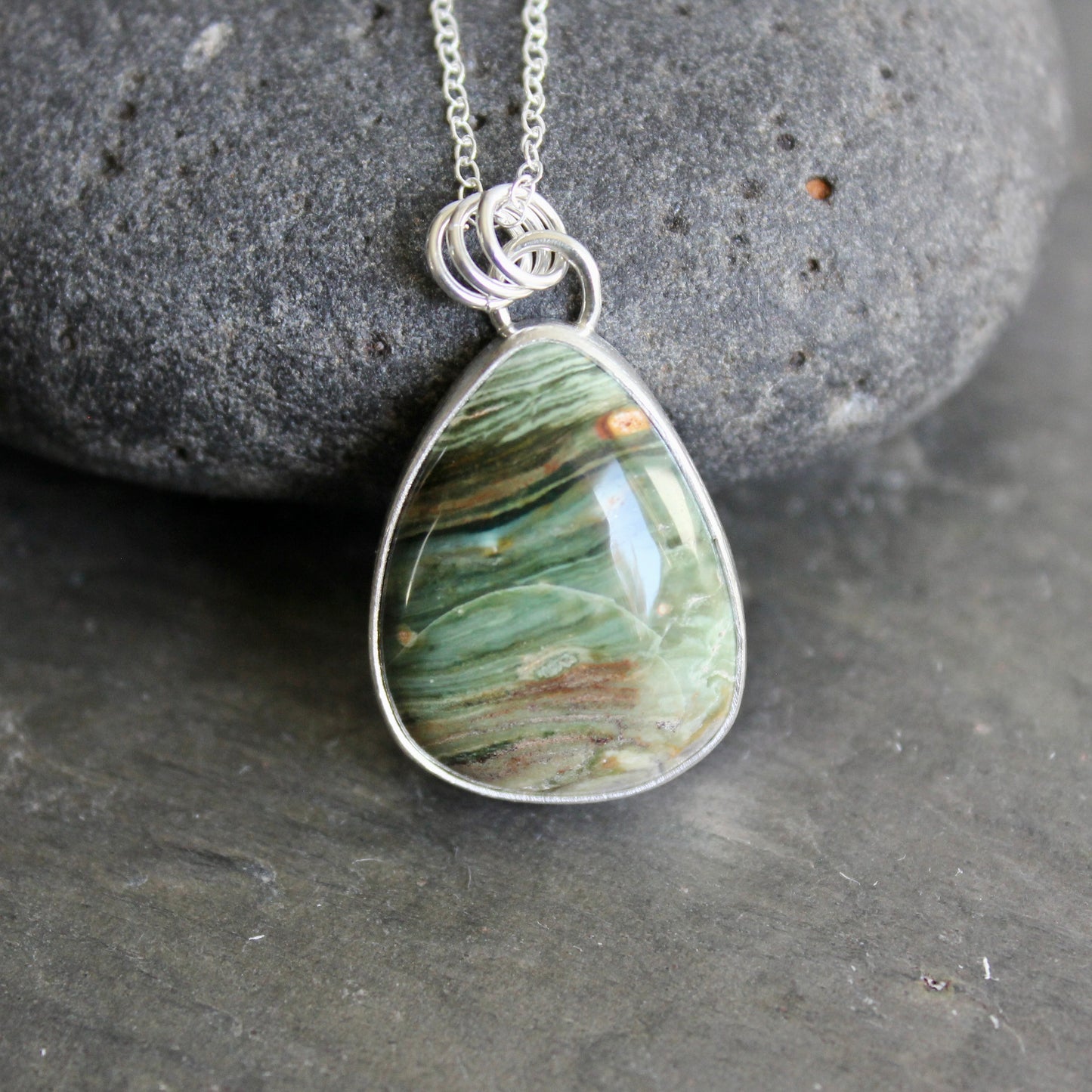 Teardrop-shaped pendant with a bezel set gary green jasper on a chain against a gray background
