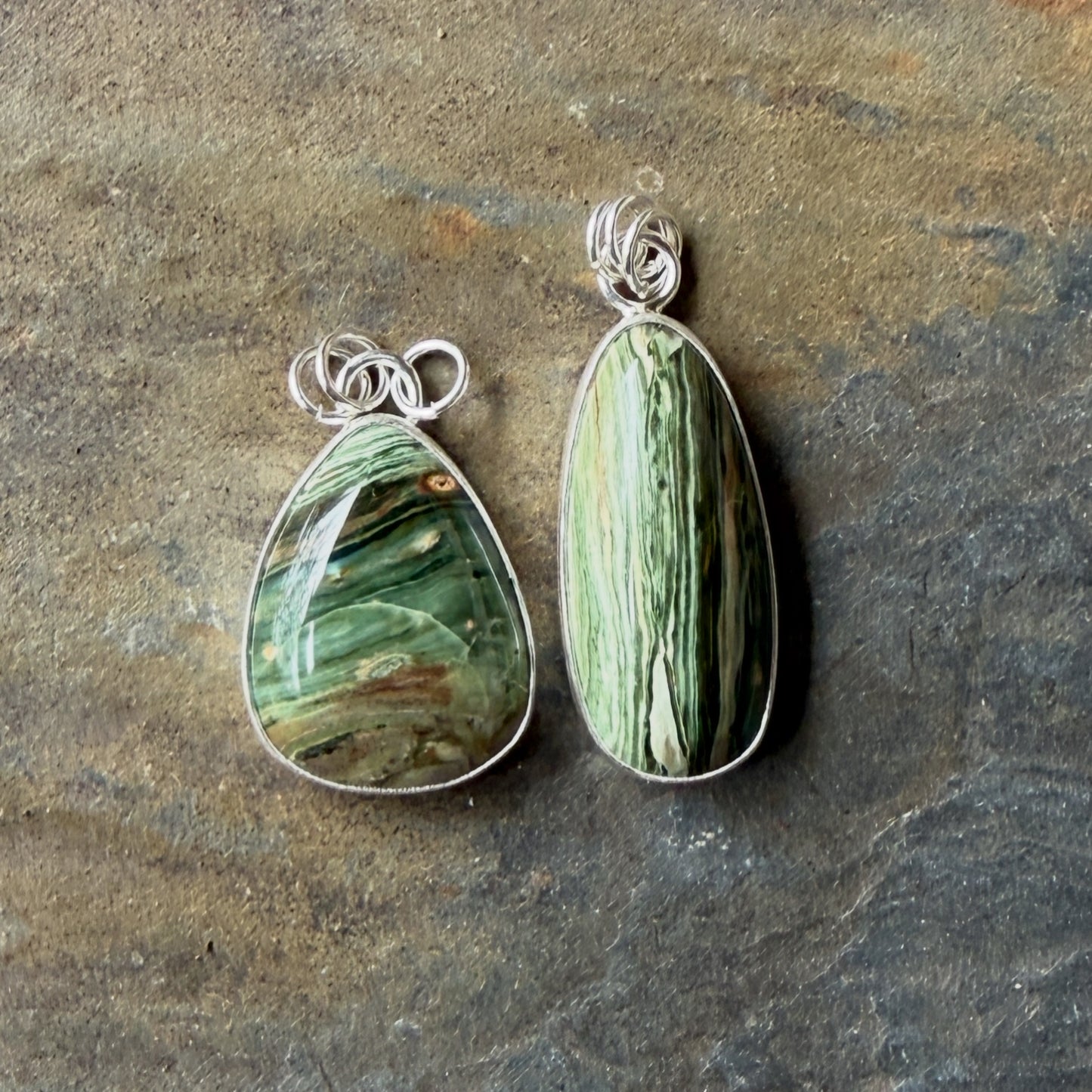 Two green stone pendants with silver wirewrapping on a stone surface