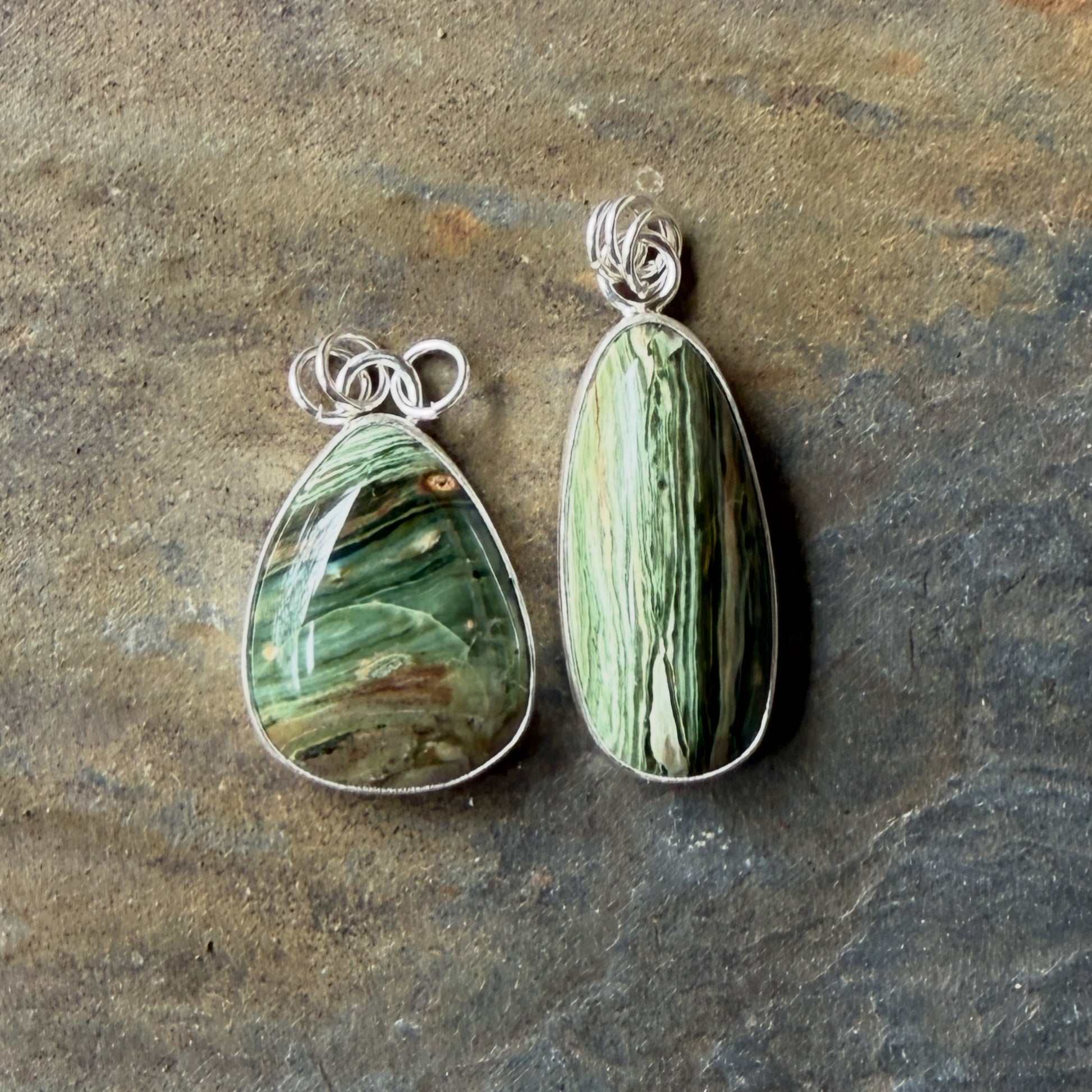 Two green stone pendants with silver wirewrapping on a stone surface
