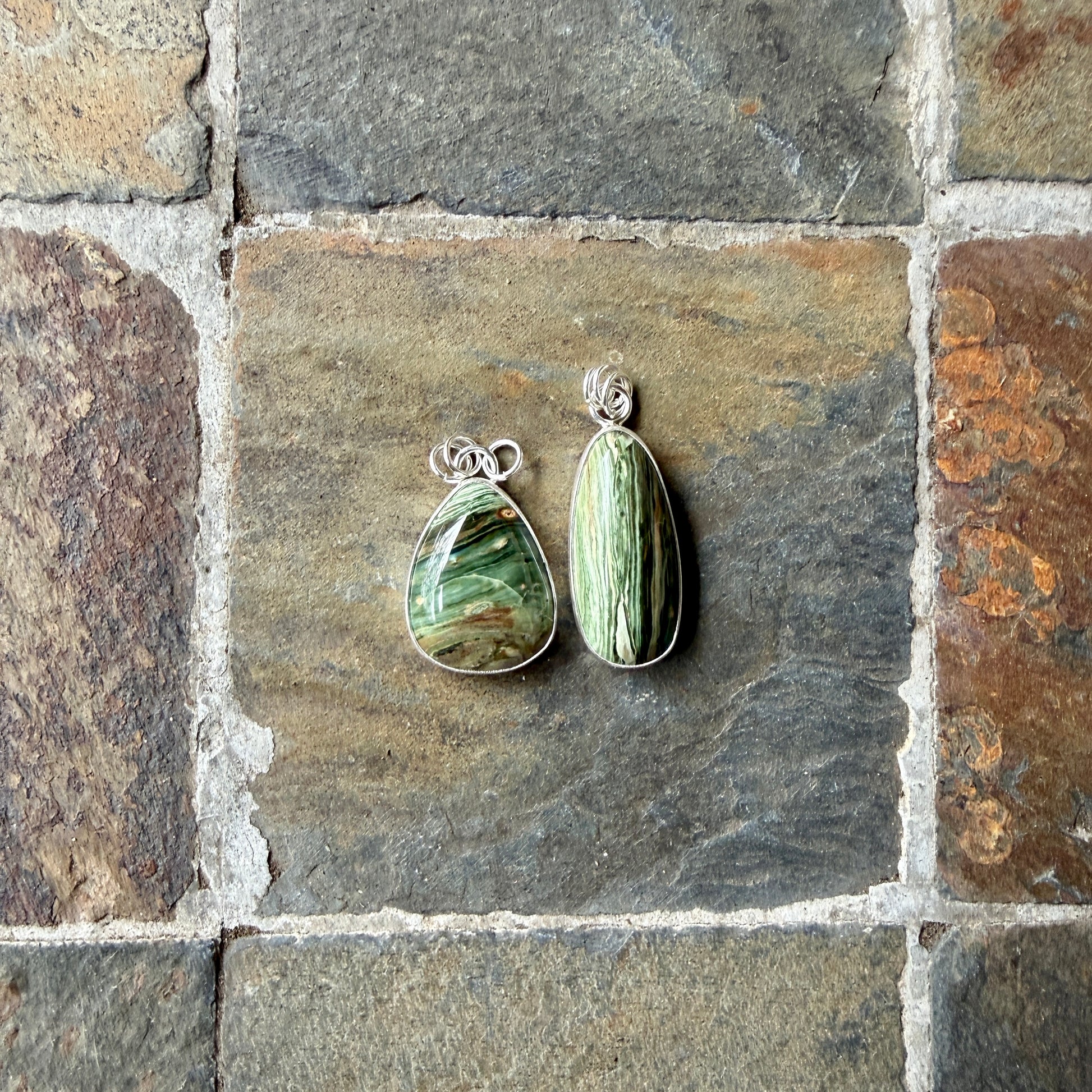 Two green stone pendants on a stone surface