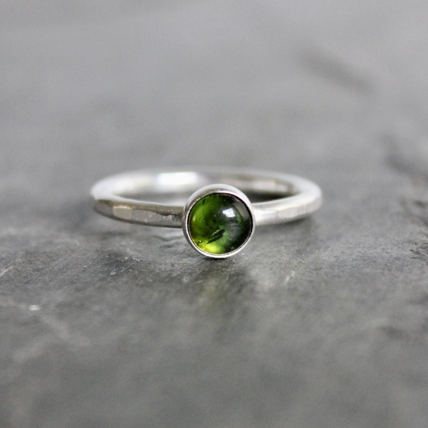 Silver ring with a green tourmaline gemstone on a gray stone surface