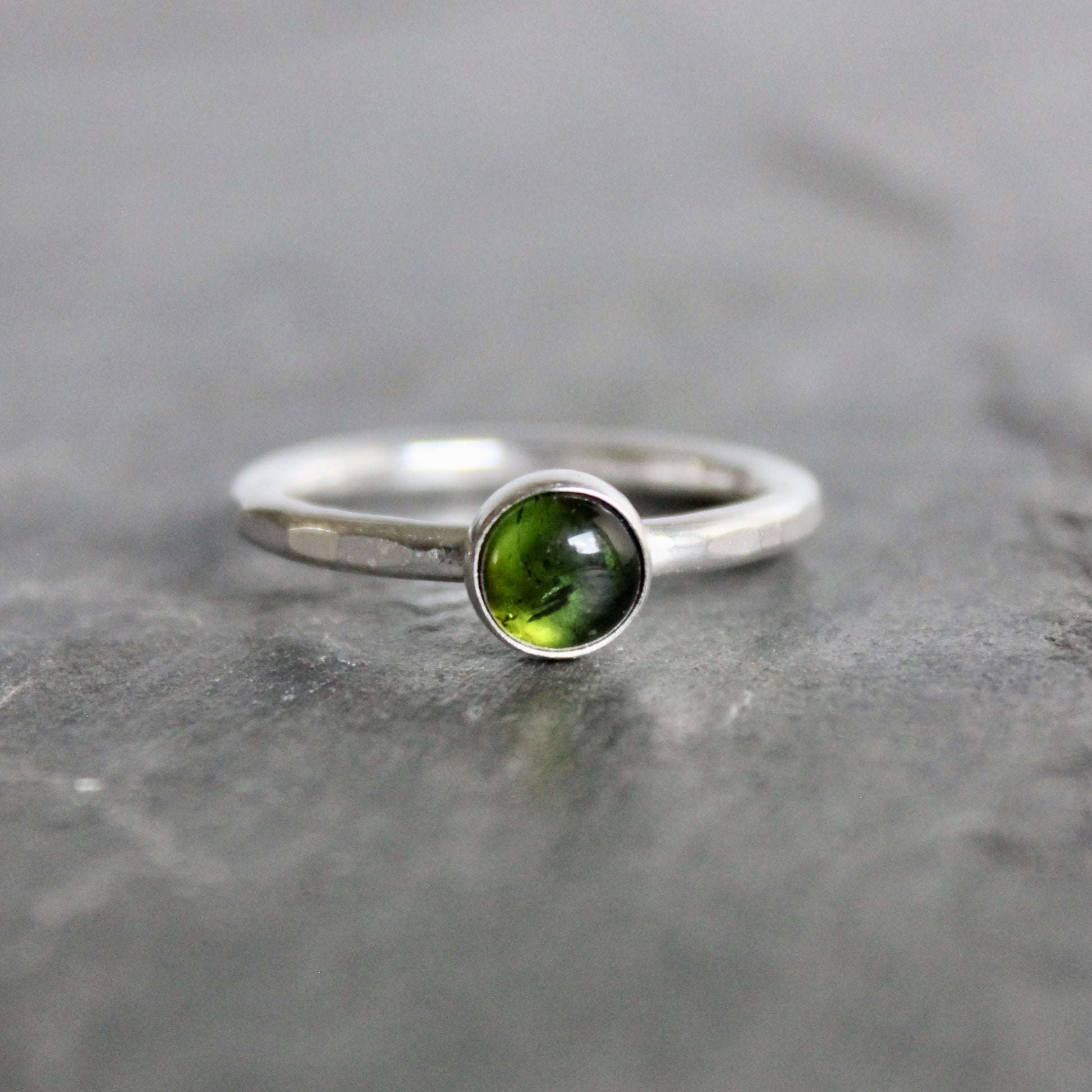 Silver ring with a green tourmaline gemstone on a gray stone surface
